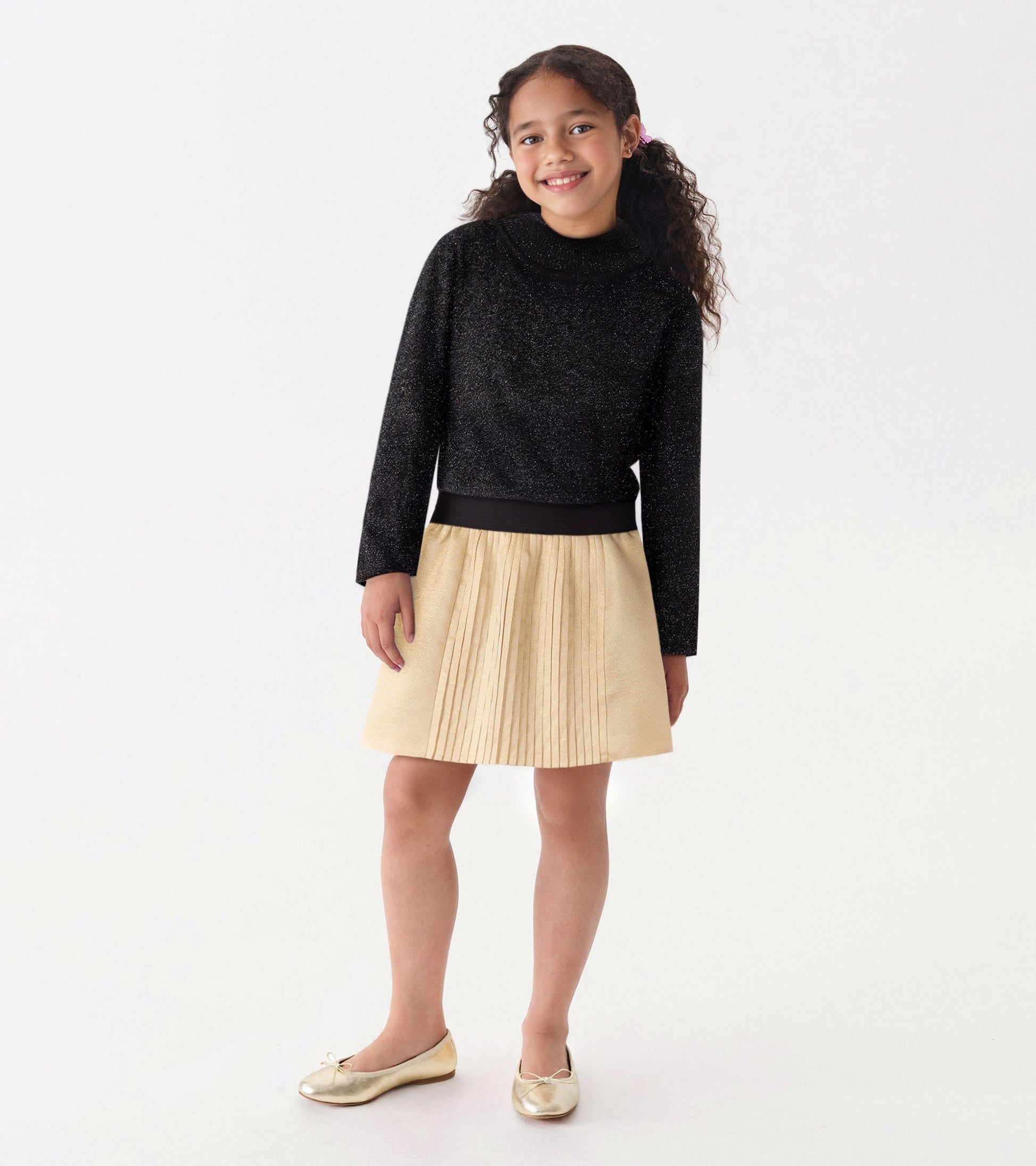 Black glitter turtleneck with long sleeves, paired with a pleated gold skirt.