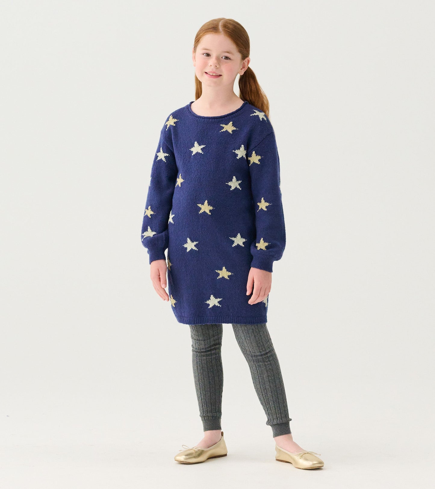 Blue sweater dress featuring gold star patterns, long sleeves, and a relaxed fit, paired with gray leggings and gold shoes.