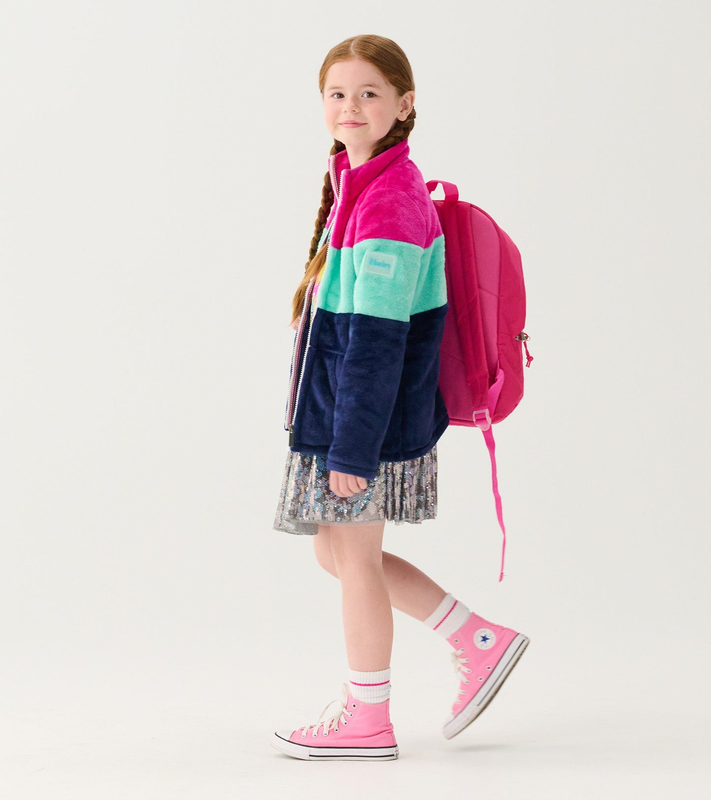 Fuzzy fleece zip-up jacket featuring colorblock stripes in pink, teal, and navy, worn by a girl with a pink backpack.