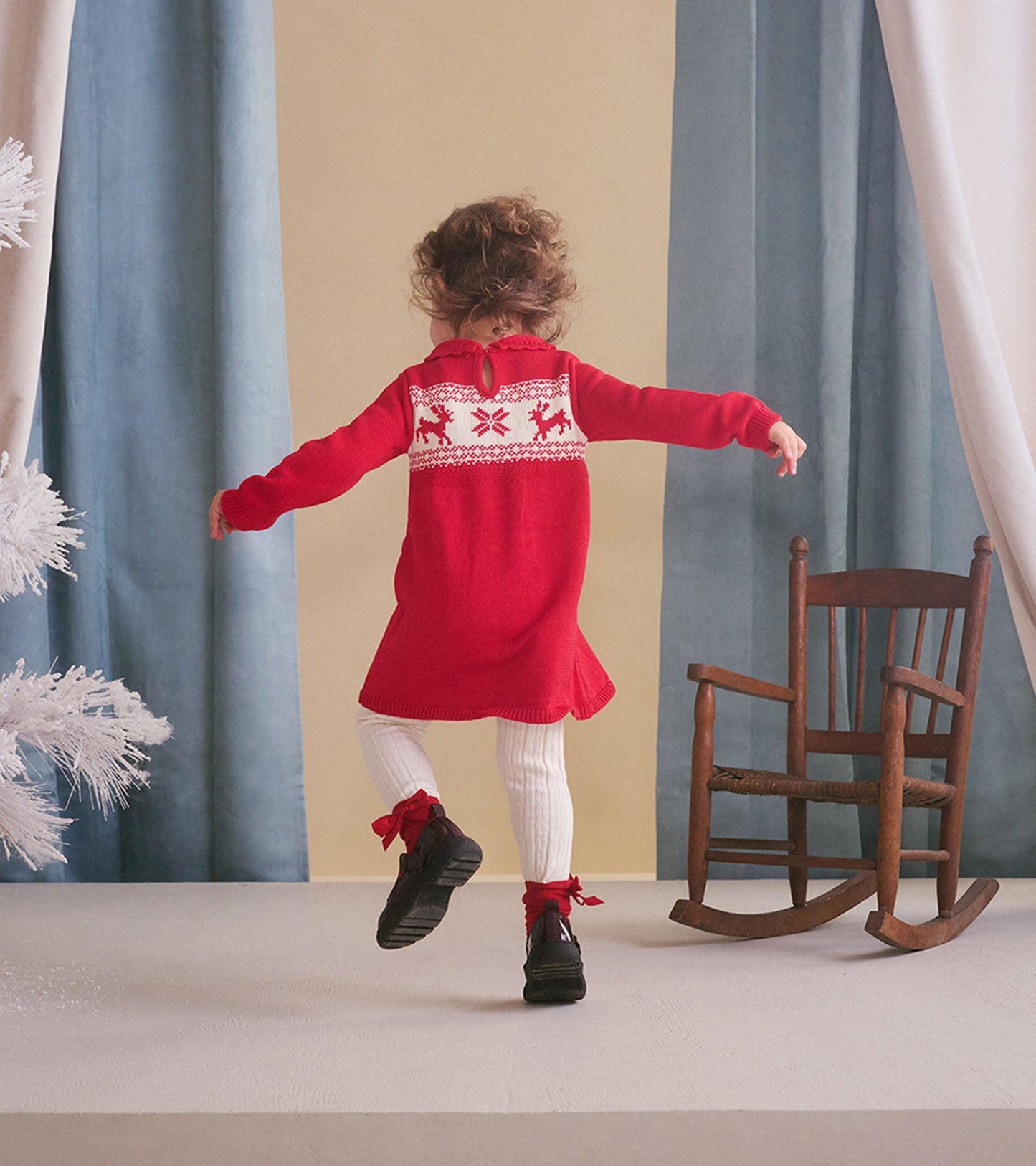 Red cable knit sweater dress with festive pattern on the back, paired with white tights and black shoes.
