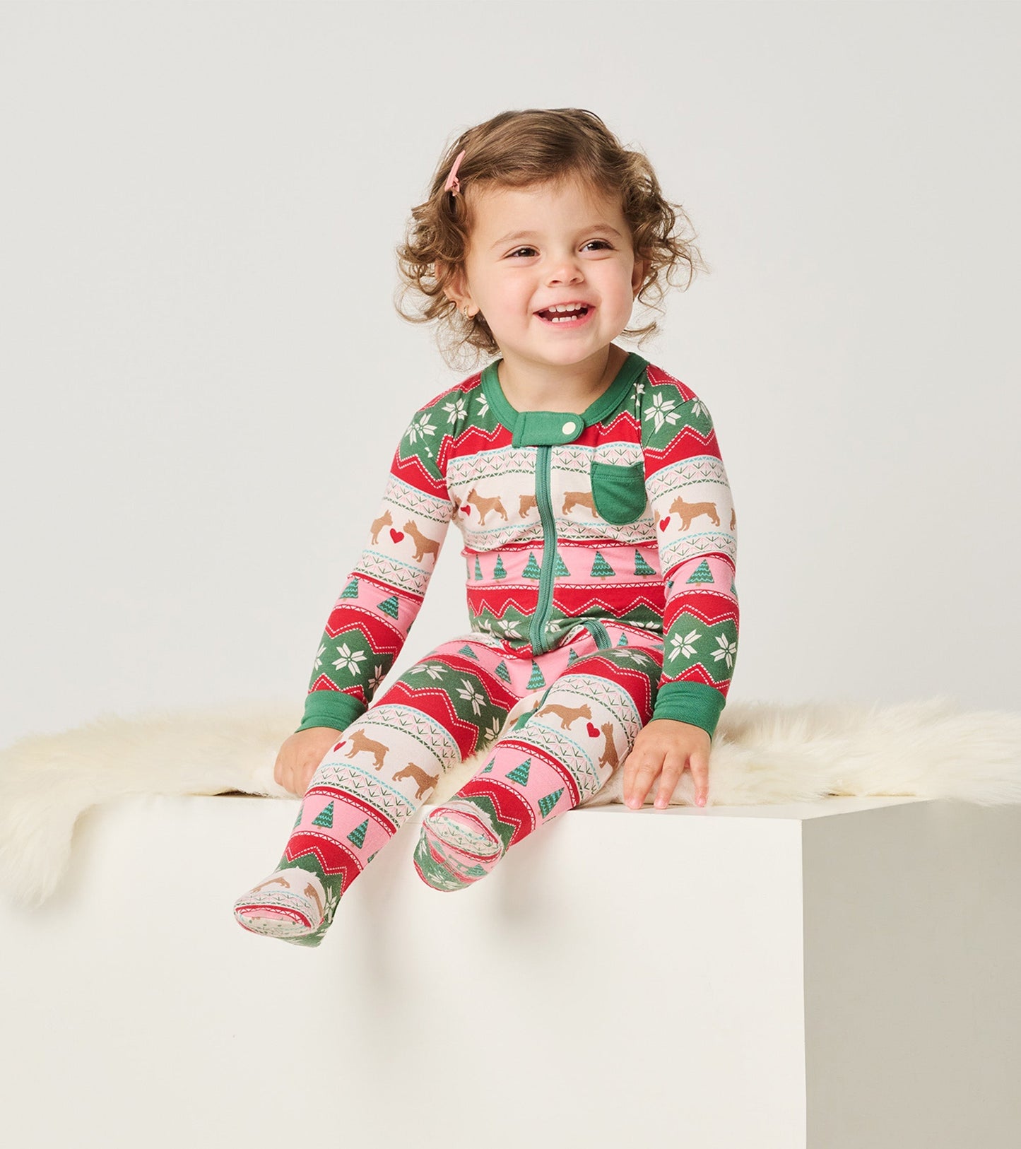 Colorful bamboo footed sleeper with puppy and heart patterns, featuring a green collar and a front pocket, worn by a smiling…