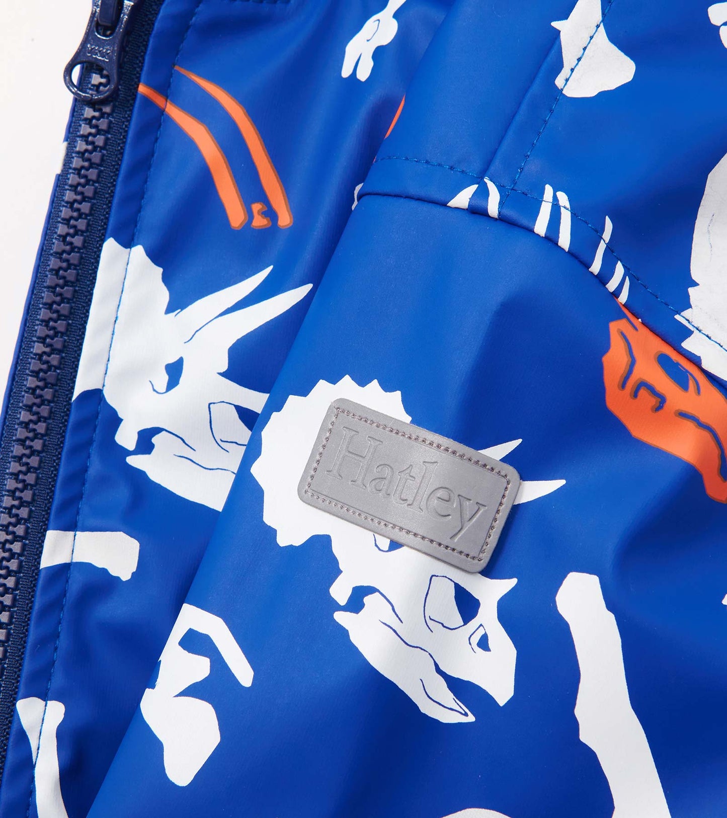 Blue zip-up raincoat featuring white and orange dinosaur fossil patterns. Includes a logo patch on the front.