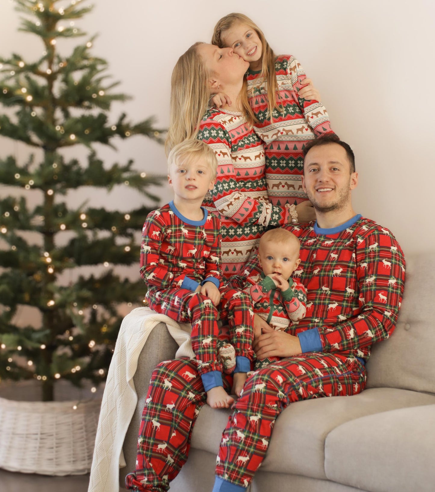 Red plaid pyjama set featuring elk and holiday patterns, worn by a family sitting together on a couch.
