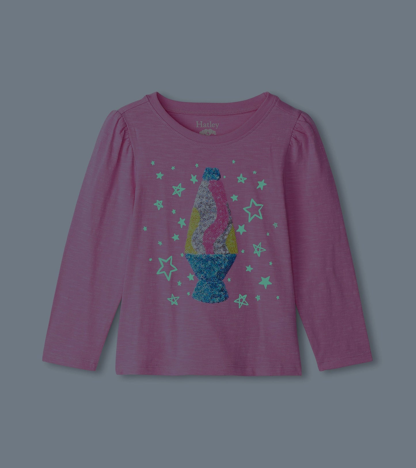 Pink long sleeve tee featuring a colorful lava lamp graphic surrounded by stars. Soft fabric with gathered shoulder detail.
