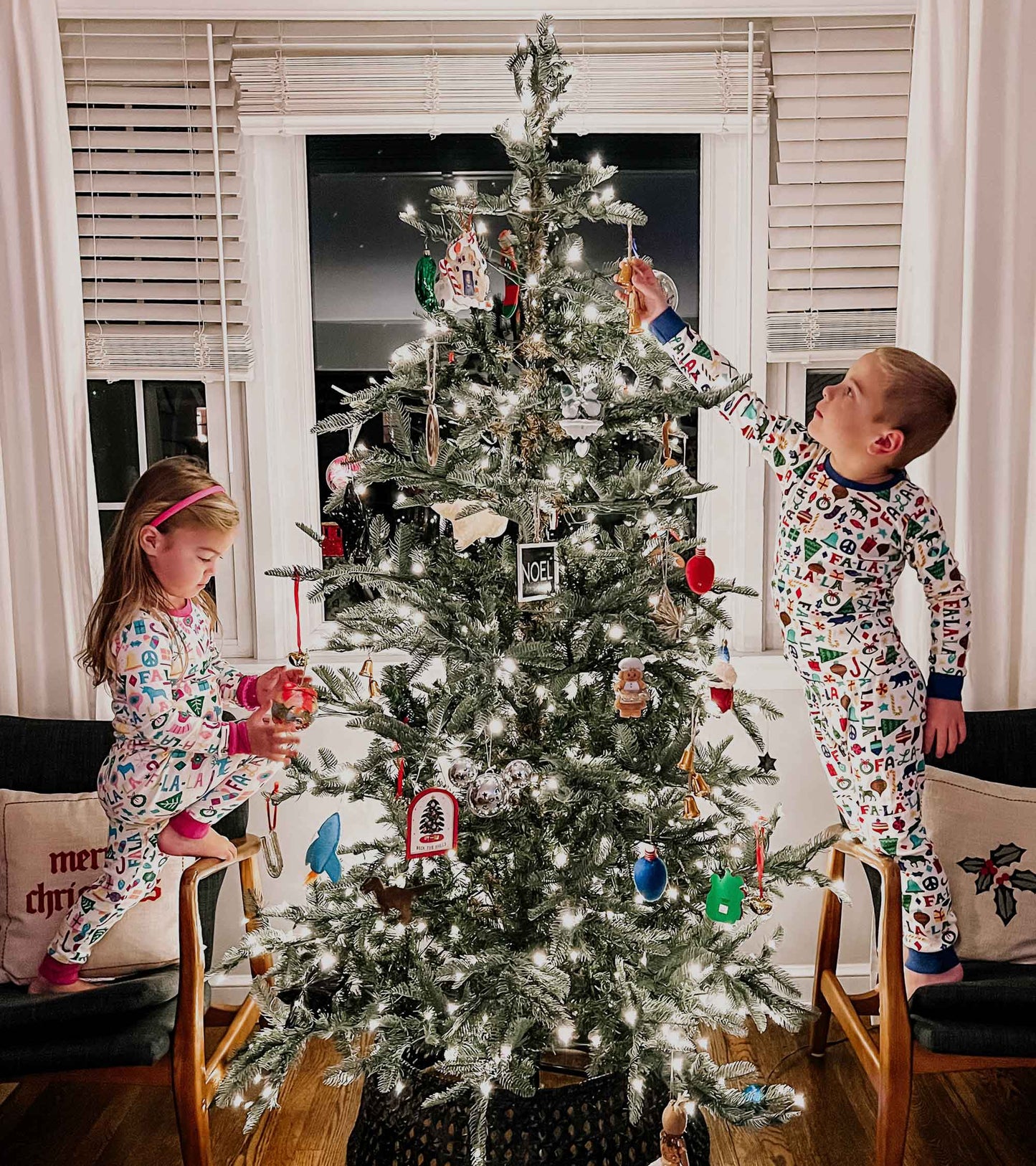 Colorful, patterned pink pyjama set worn by children, featuring festive designs, while decorating a Christmas tree.
