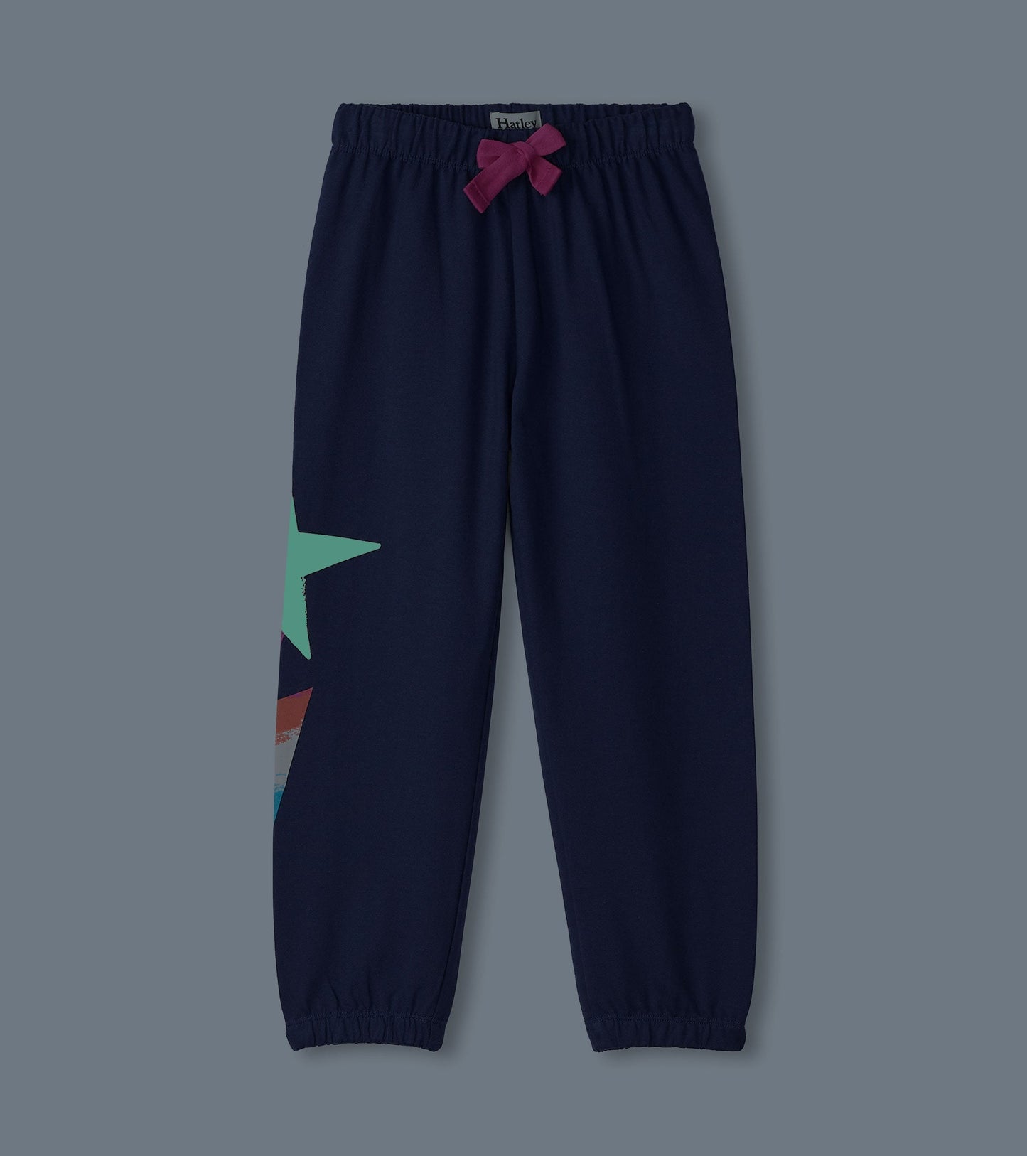 Navy baggy track pants with a star graphic and a pink bow at the waistband, featuring elastic cuffs for a relaxed fit.