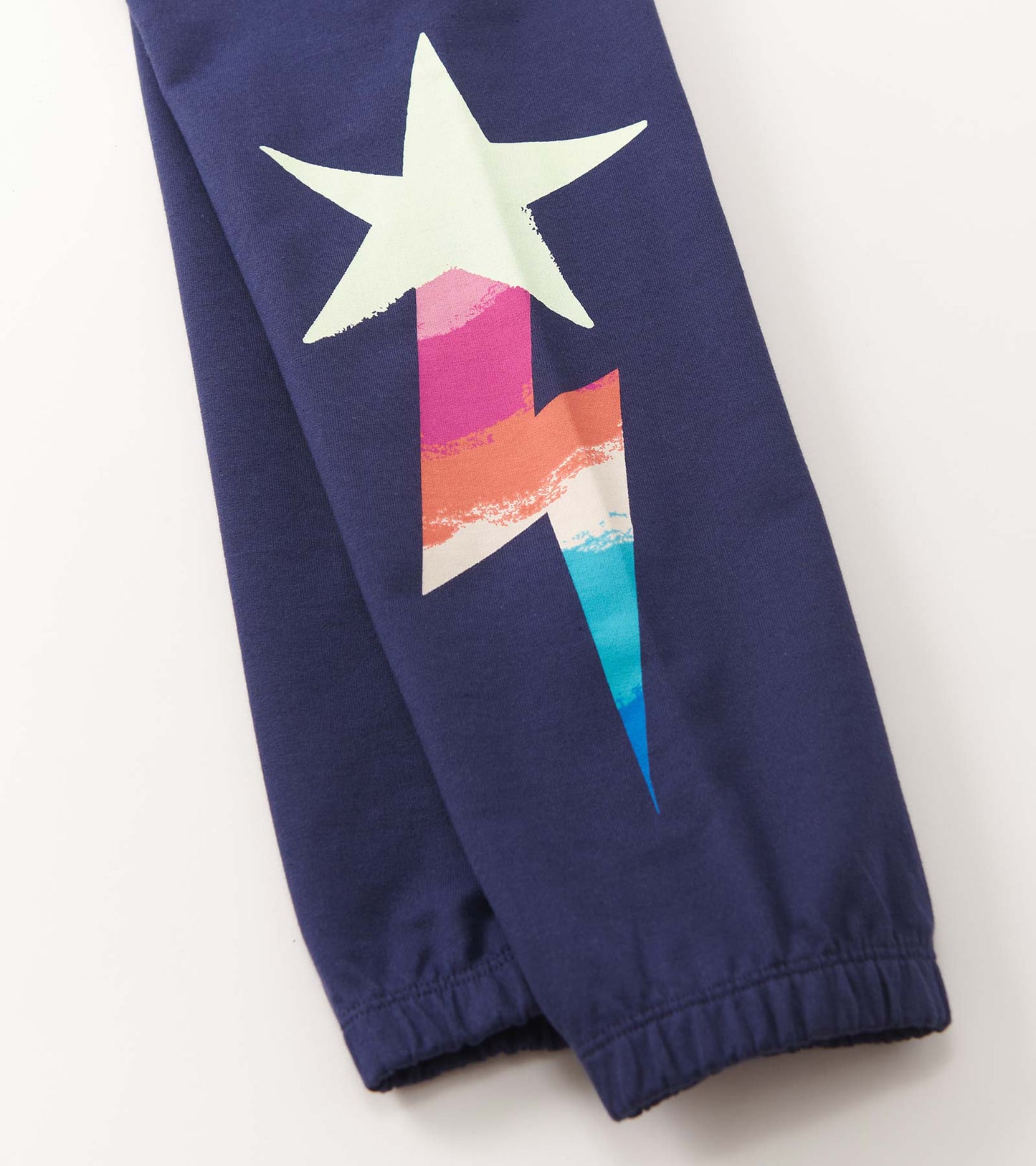Navy baggy track pants featuring a colorful star and lightning bolt graphic on the side. Elastic cuffs for comfort.