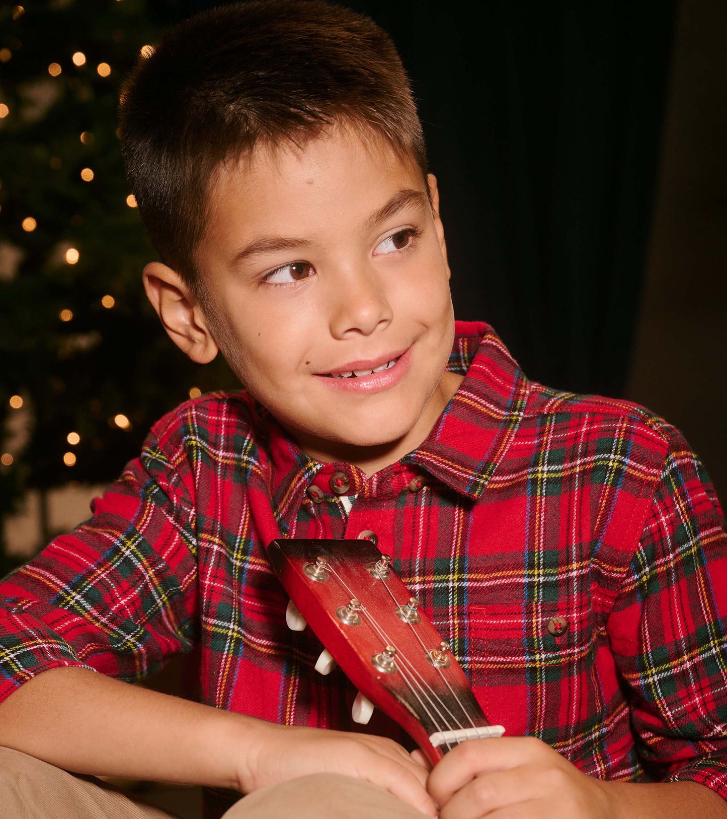 Red plaid button-down shirt with a collar, featuring green and yellow accents, worn by a boy holding a ukulele.