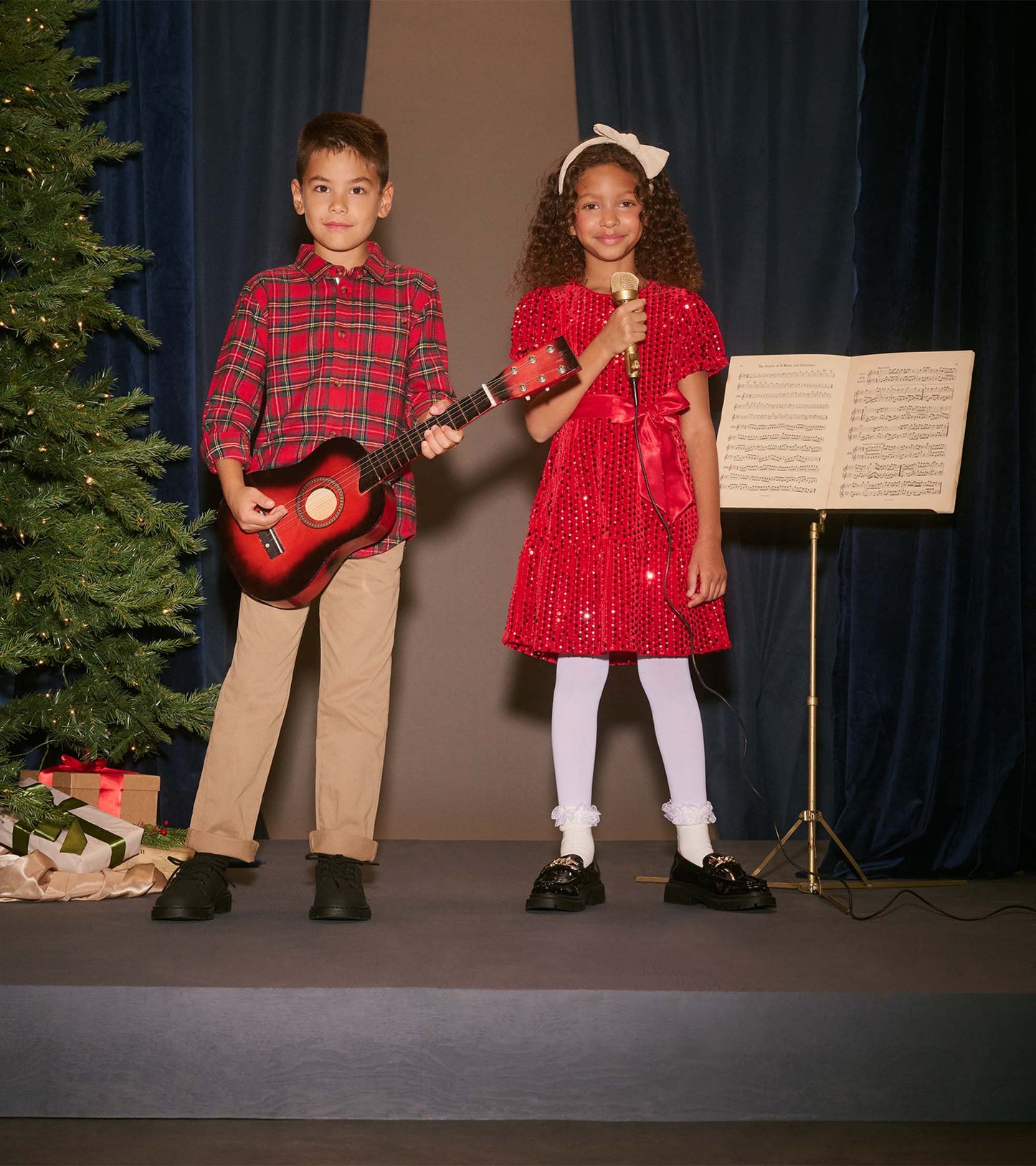 Boys red plaid button-down shirt with long sleeves, worn by a child holding a guitar, paired with beige pants.