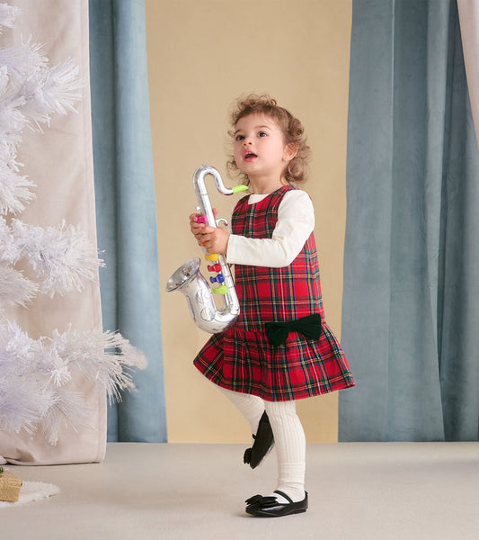 Red plaid pinafore dress with a flared skirt and bow detail, worn over a long-sleeve white shirt by a toddler.