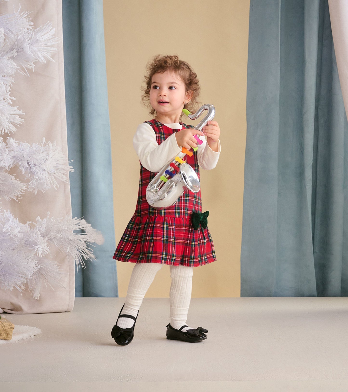 Red plaid pinafore dress with a flared skirt, worn over a long-sleeve white shirt, paired with white tights and black shoes.