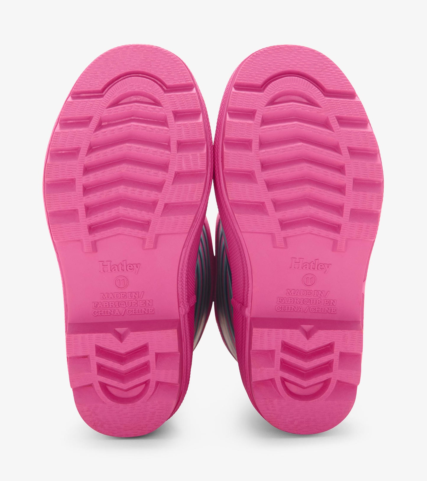 Pink rubber soles of girls' wellies with violet stripes, designed for wet weather and outdoor play.
