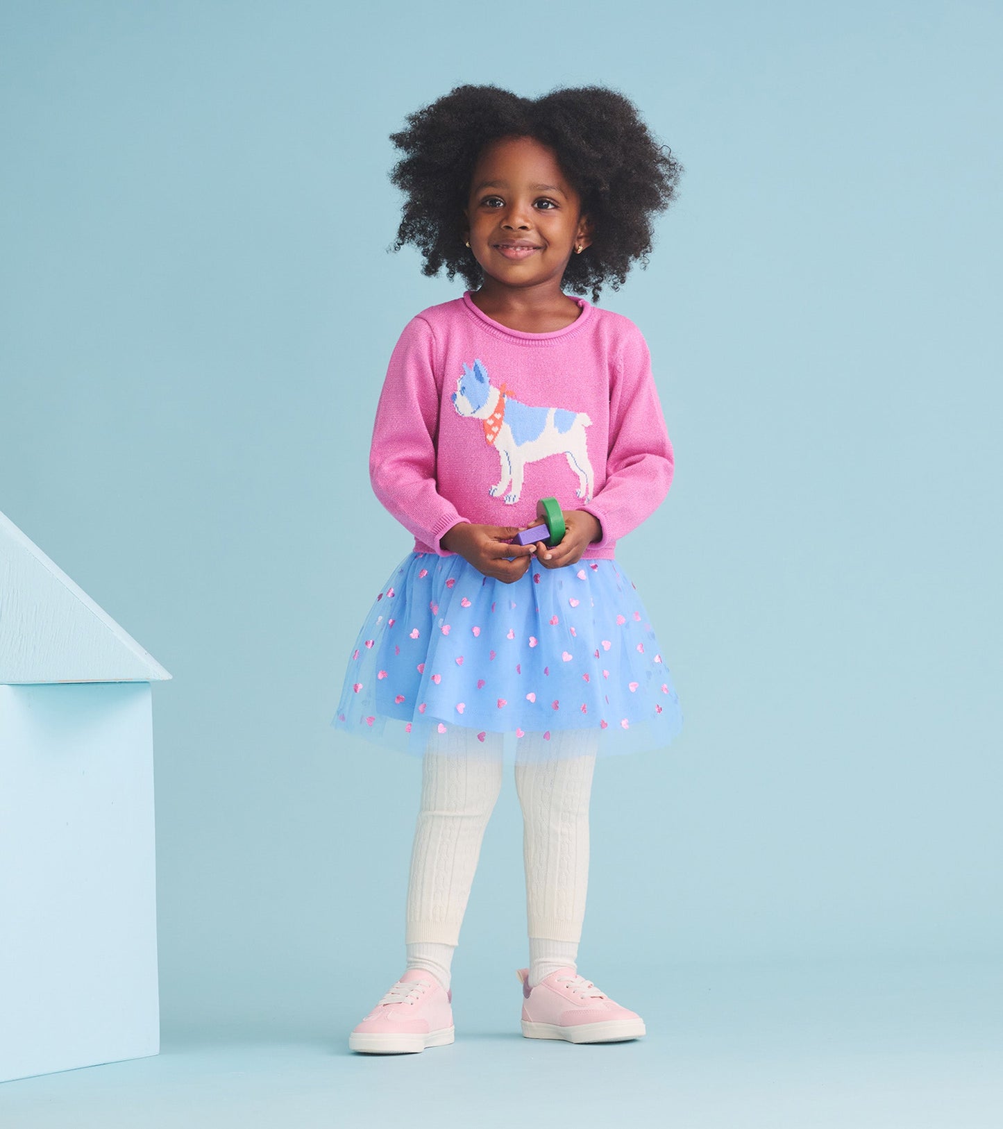 Pink sweater dress with French bulldog design, layered tulle skirt in blue with pink hearts, worn with white tights and pink…