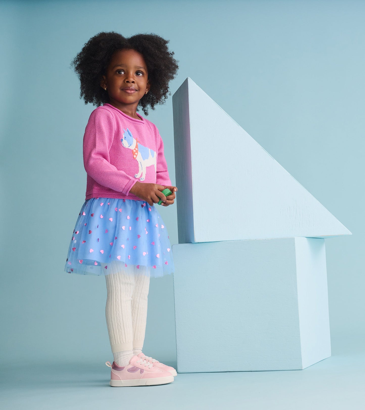Pink sweater dress with French bulldog design, layered tulle skirt, and white tights, worn by a girl standing beside a blue…
