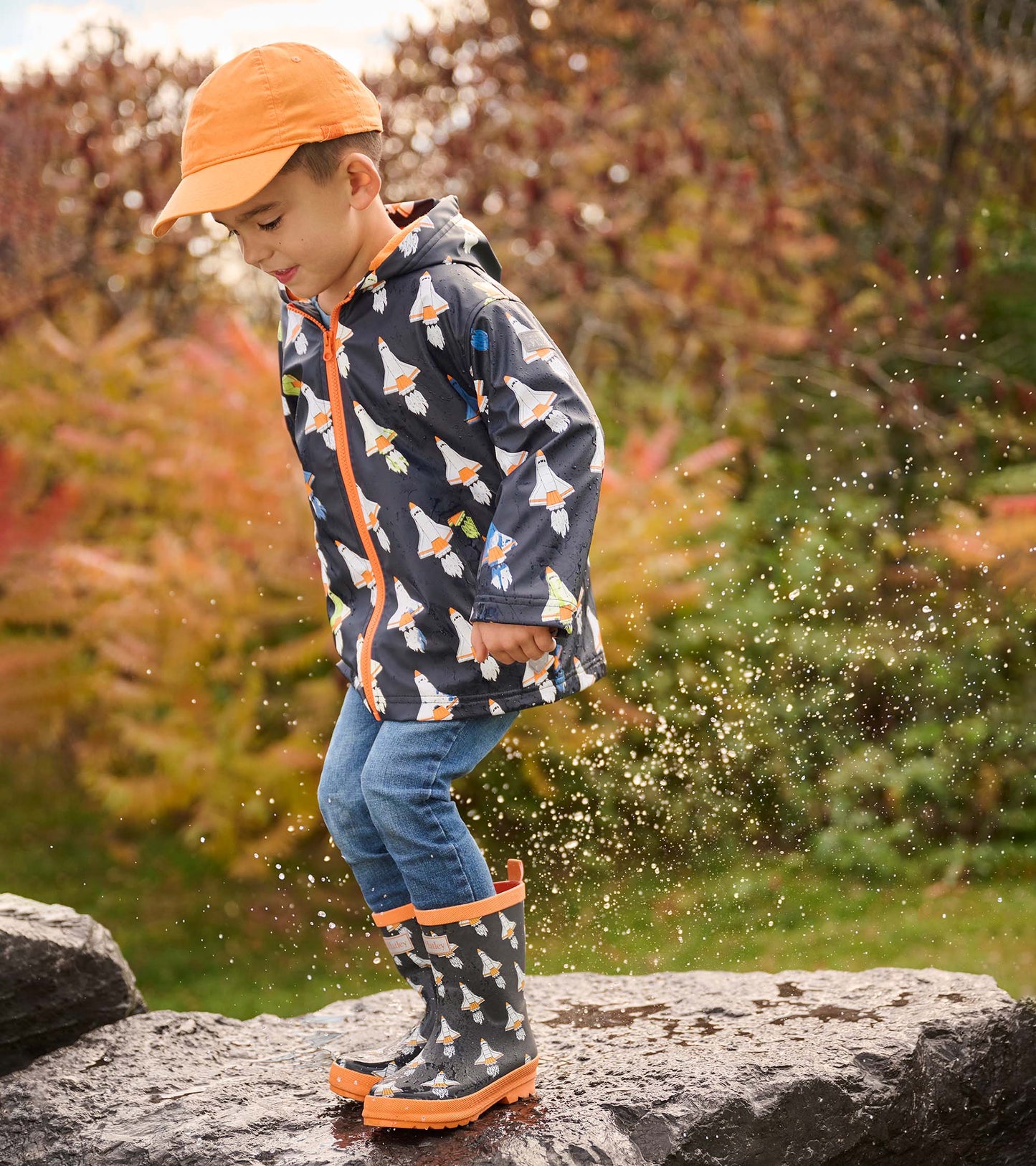 Matte black wellies with colorful space shuttle pattern and orange trim, worn by a child splashing in water.