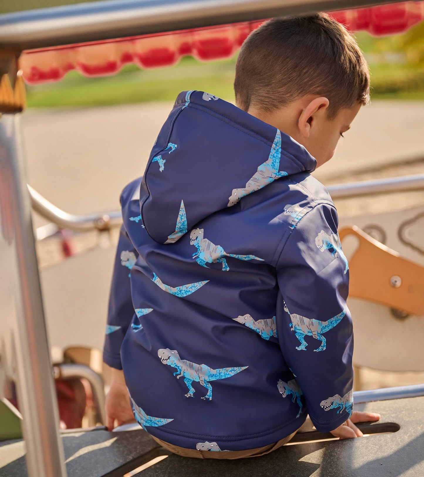 Navy raincoat with T-Rex print, hooded, and sherpa lining, worn by a child sitting on playground equipment.