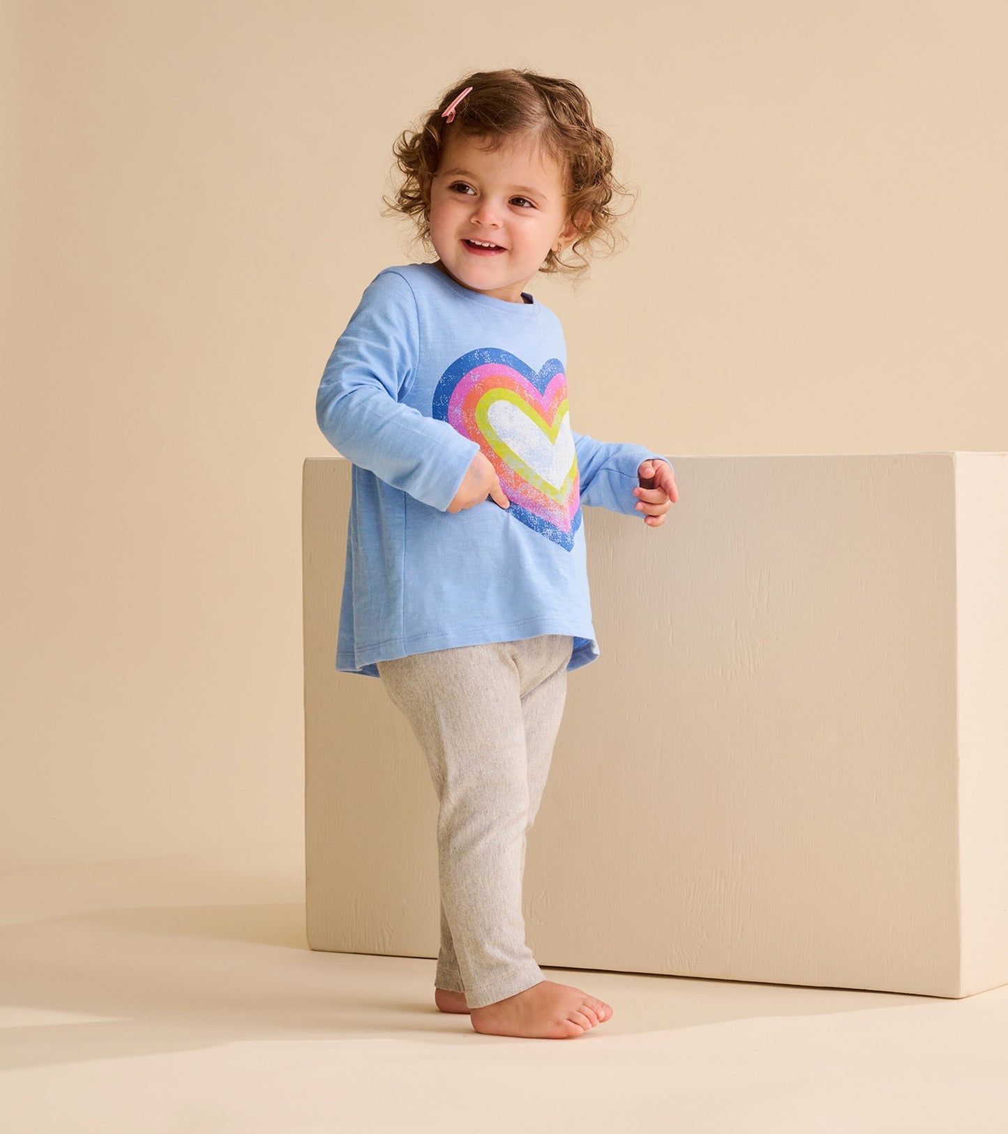 Light blue long sleeve t-shirt featuring a colorful groovy heart design, paired with gray leggings.