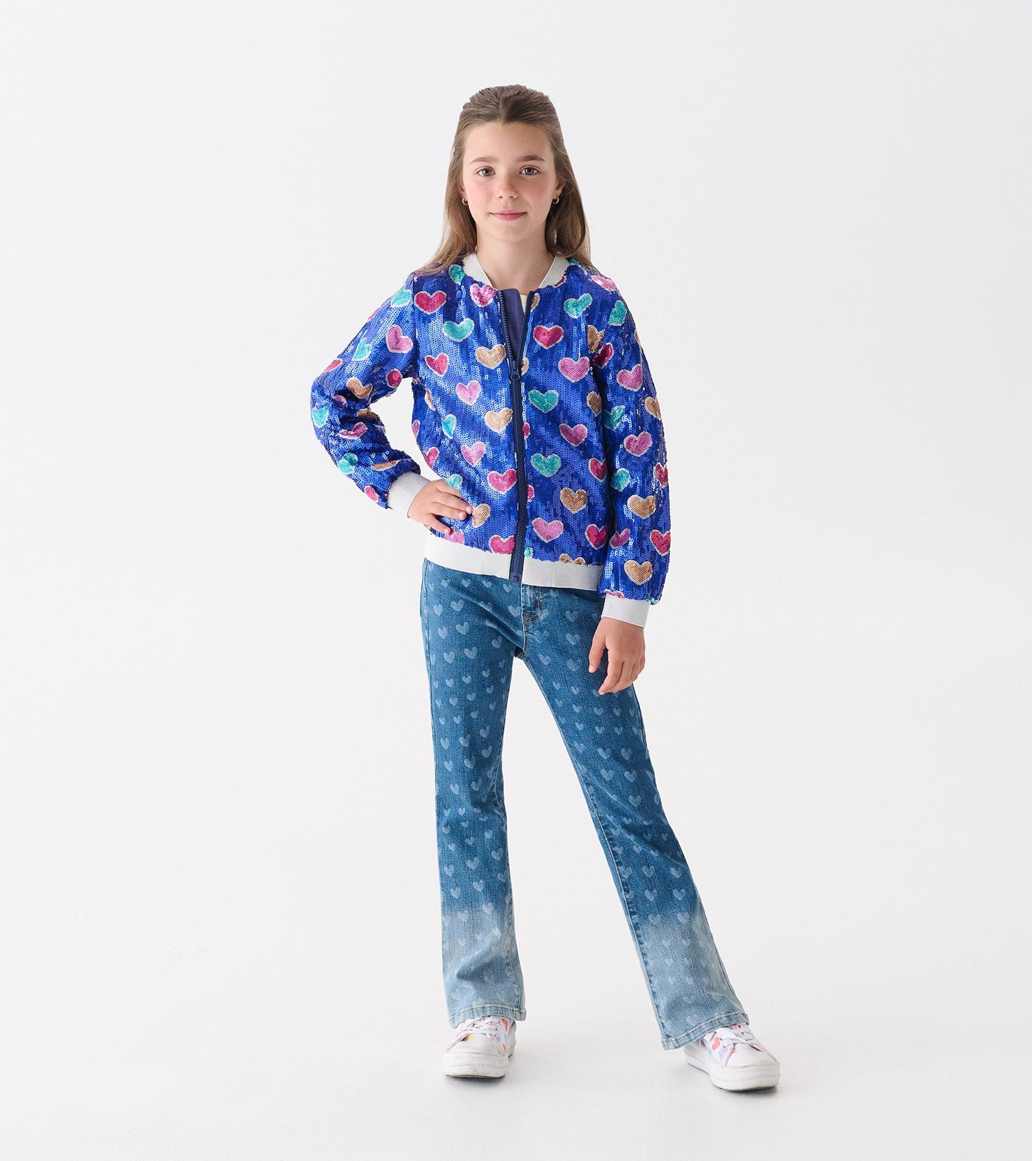 Blue bomber jacket with multicolored heart sequins, featuring a front zipper and ribbed cuffs, worn by a girl.