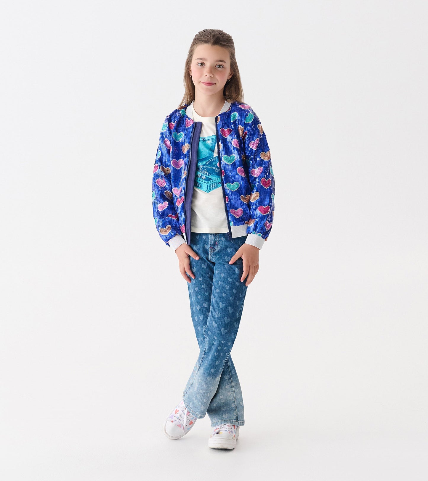 Blue bomber jacket with multicolored heart sequins, worn over a white shirt and paired with denim jeans.