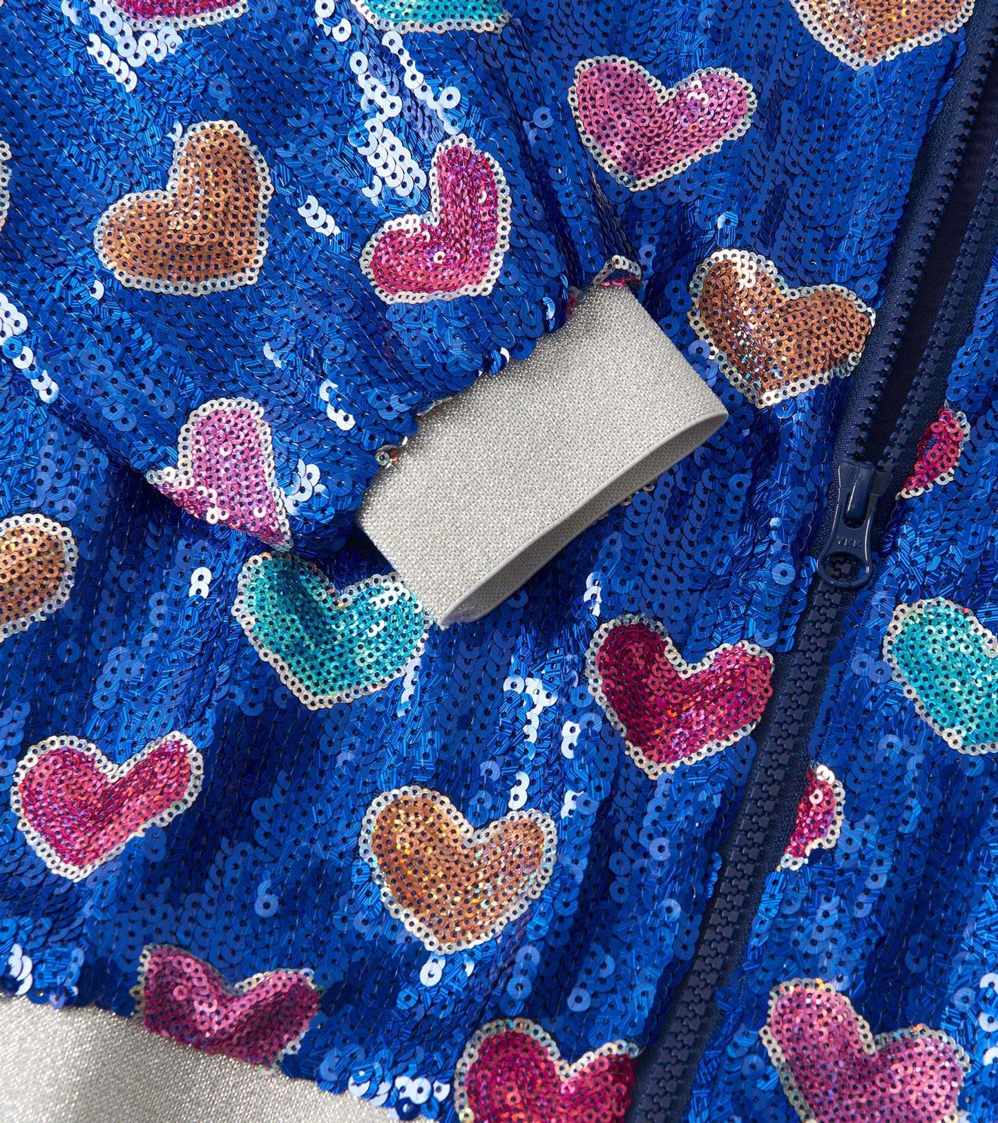 Blue sequin bomber jacket featuring colorful heart patterns and a gray ribbed cuff. Zipper closure visible.