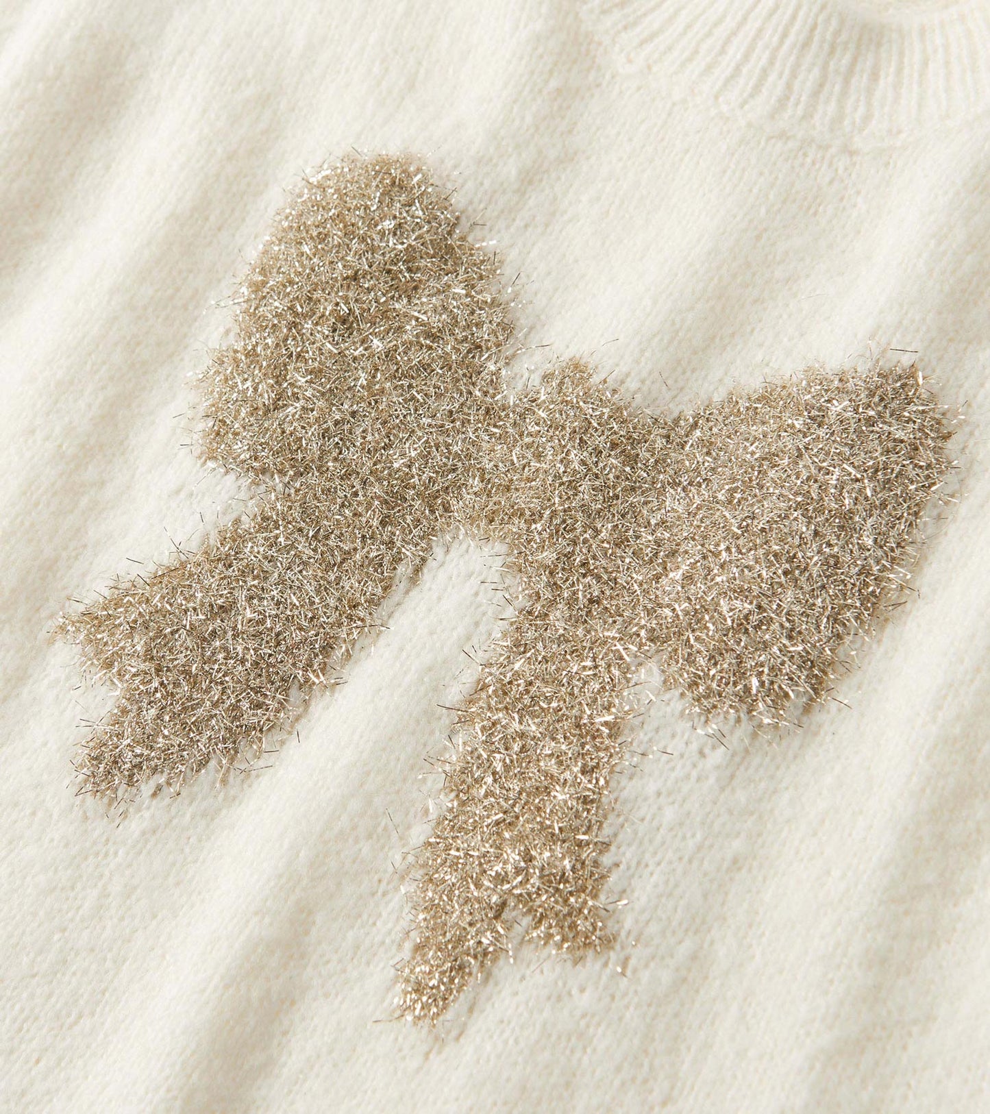 Cream sweater vest featuring a textured gold bow design on the front.
