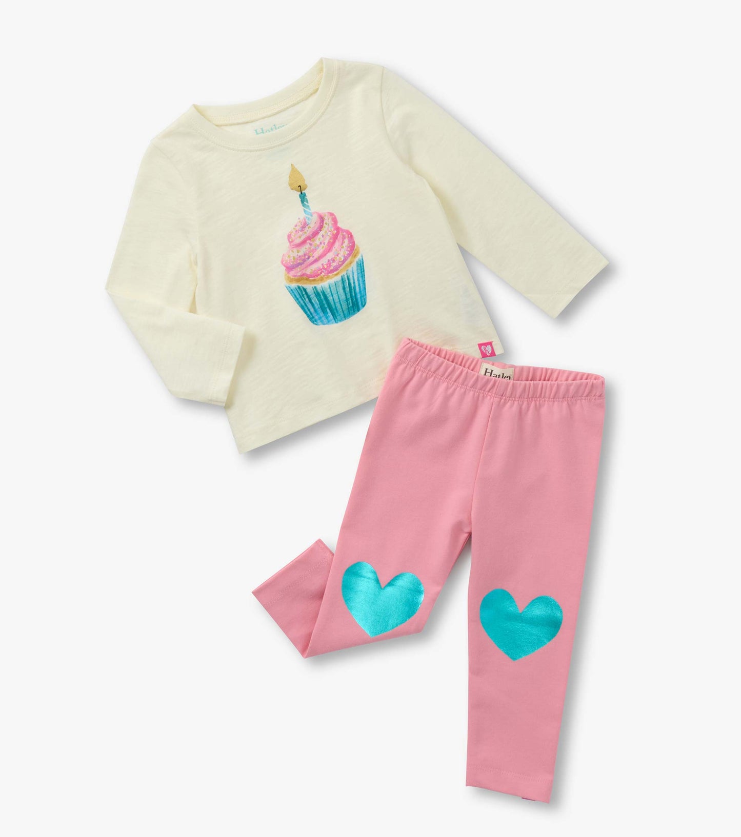 Cream long-sleeve t-shirt with cupcake graphic paired with pink leggings featuring blue heart patches.