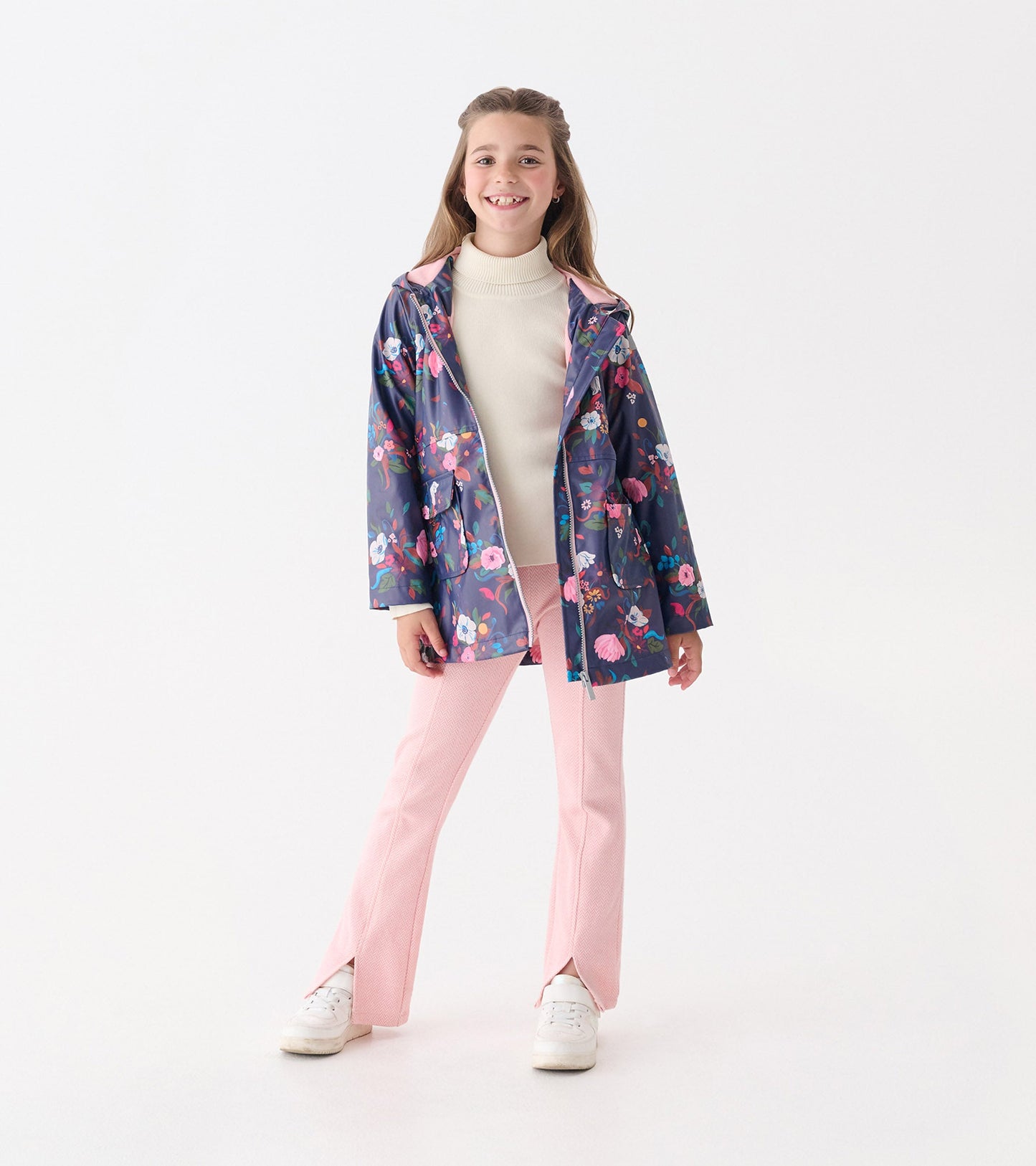 Floral zip-up raincoat in navy with pink accents, featuring a hood and pockets, worn over a cream top and pink pants.