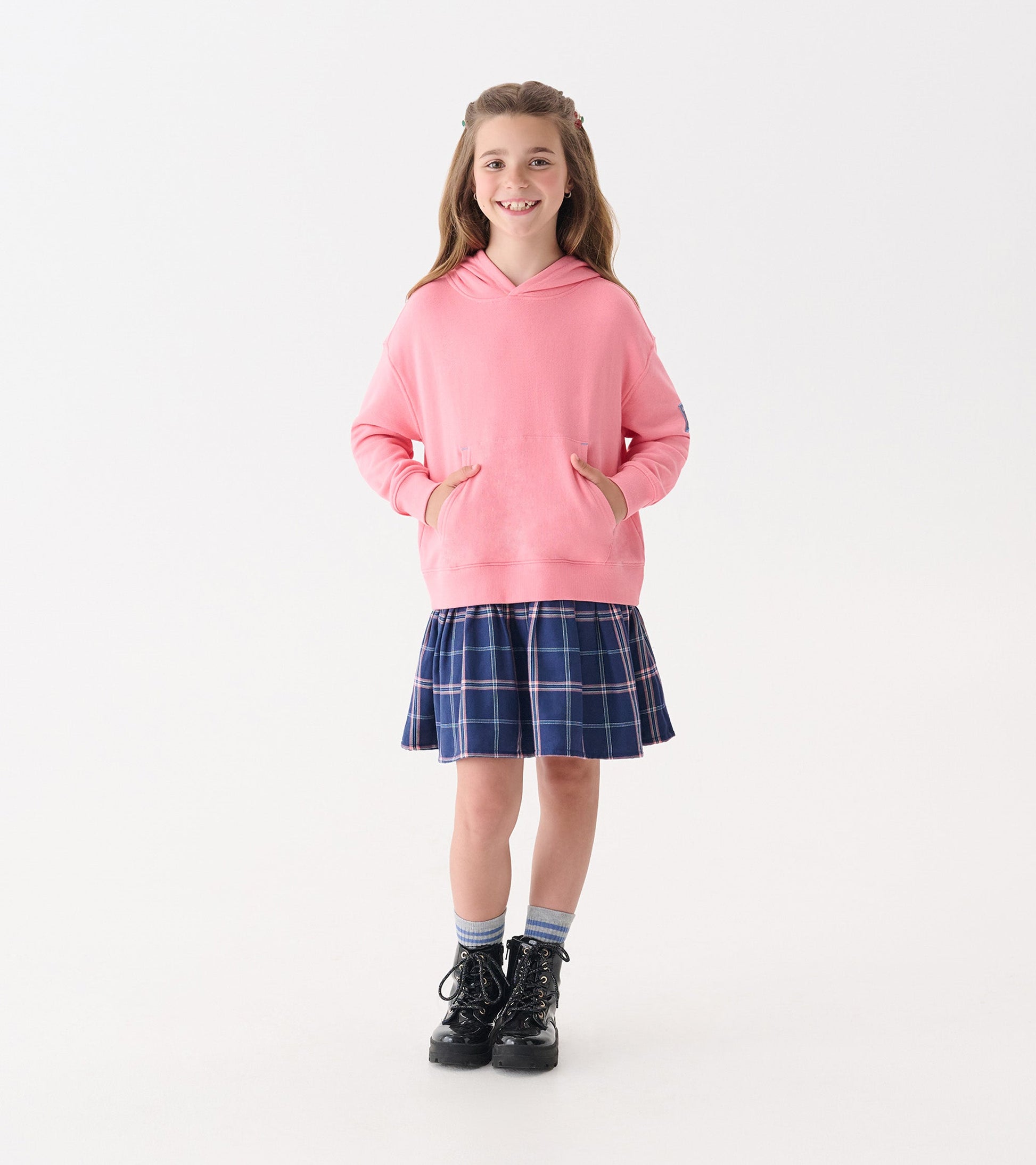 Pink hooded sweatshirt paired with a navy plaid skirt, worn with black boots and blue striped socks.