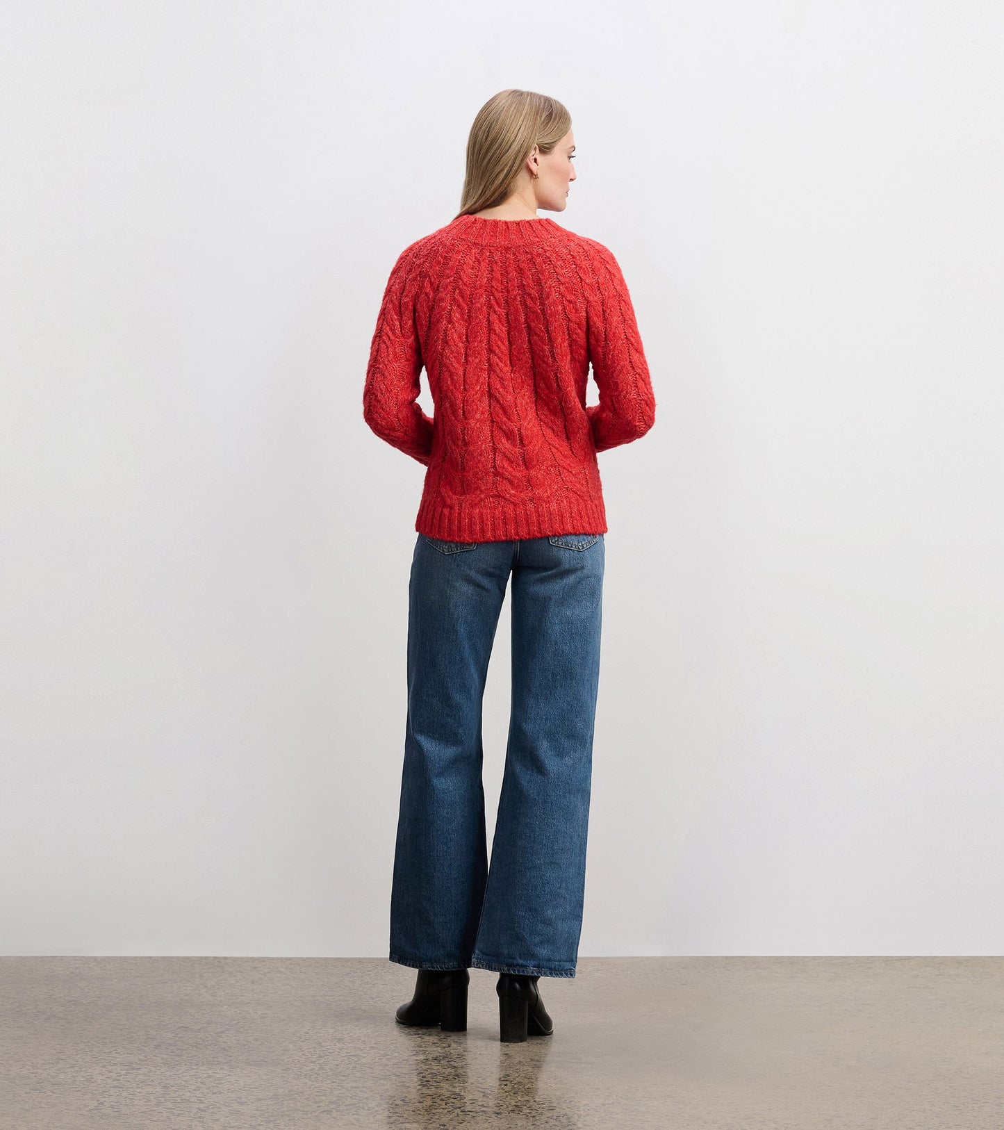 Red cable knit jumper with a relaxed fit, featuring a round neckline and long sleeves, worn with wide-leg jeans.