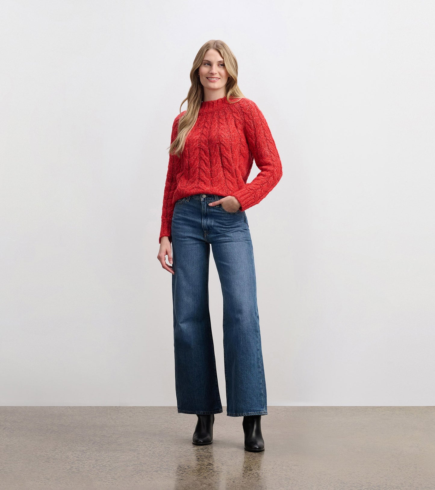 Red cable knit jumper with a round neckline, paired with wide-leg jeans and ankle boots, styled for a casual look.