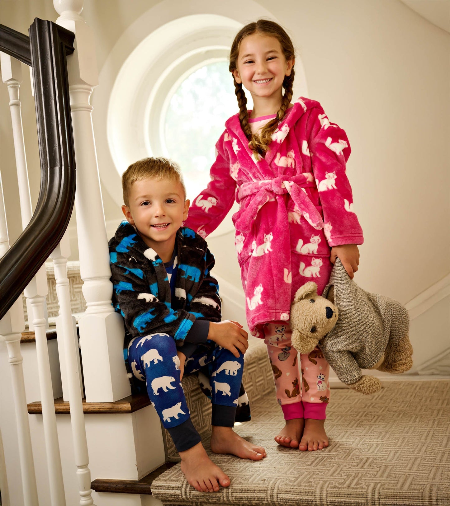 Fuzzy pink fleece robe with white kittens, worn by a girl, paired with a boy in a black robe and bear-patterned pants.