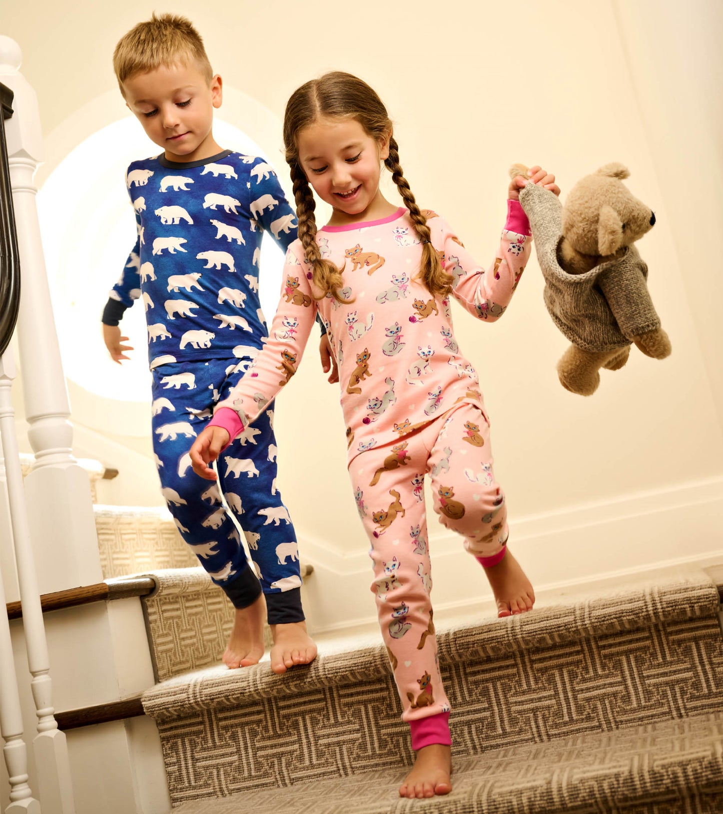 Boys' bamboo pyjama set featuring a blue polar bear print and a pink animal pattern, worn by children on stairs.