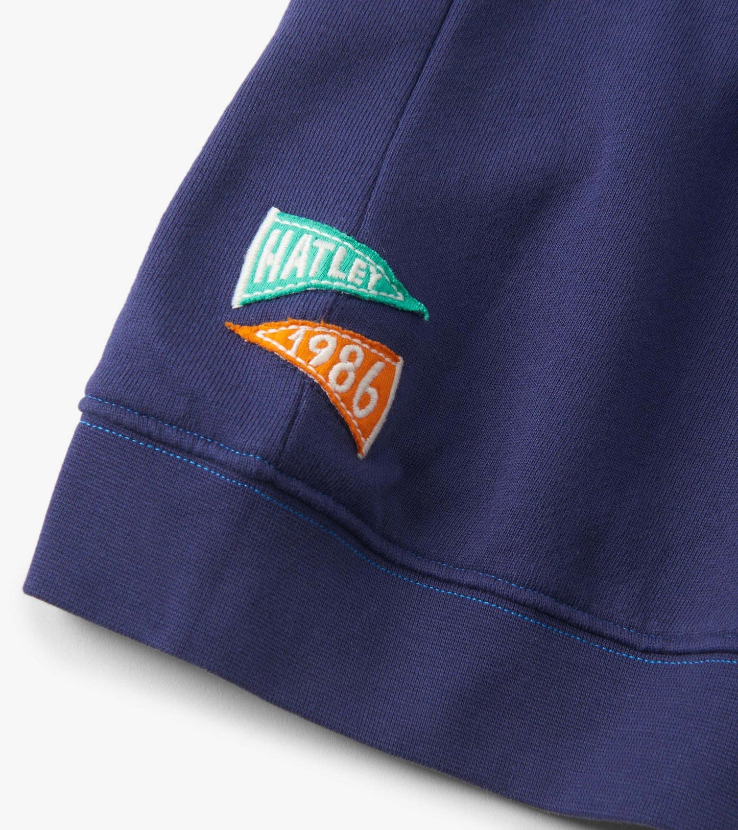 Patriot blue pullover with embroidered patches in green and orange, featuring a ribbed hem and soft fabric.