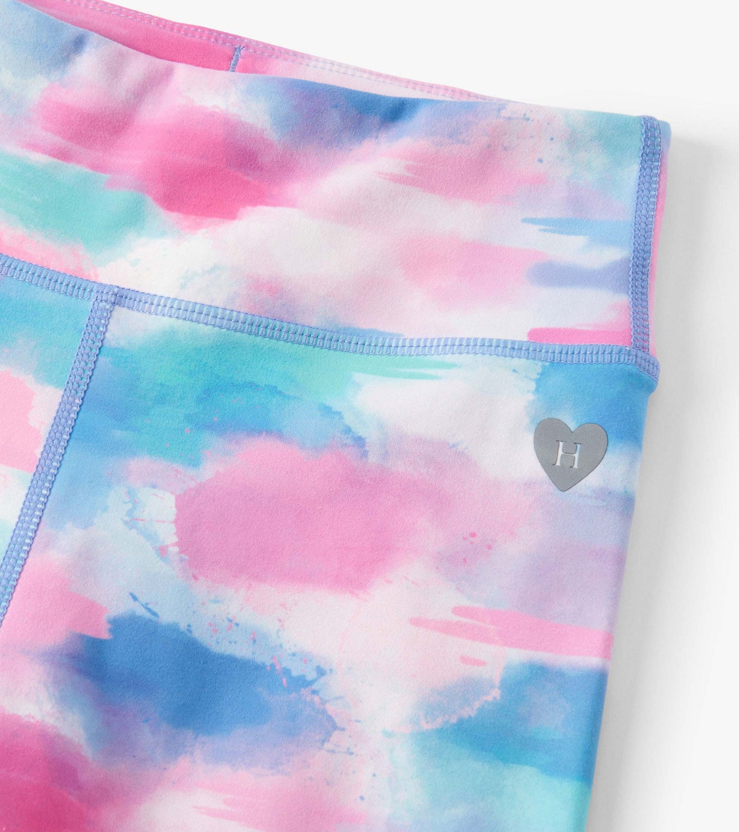 Colorful leggings featuring a watercolor pattern in pink, blue, and green with a heart logo detail.