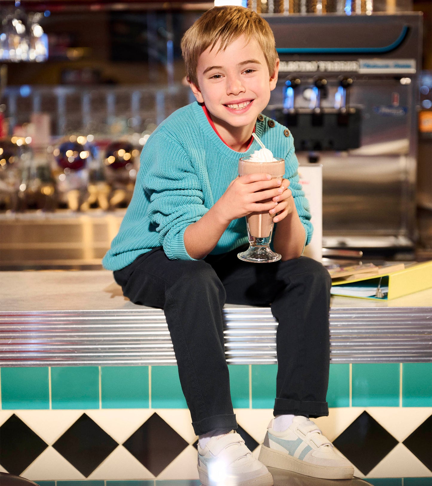 Teal button neck sweater with textured knit, worn by a boy sitting and holding a milkshake in a diner setting.