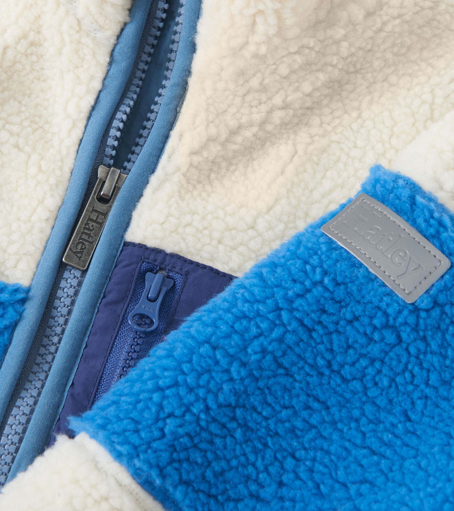 White faux sherpa zip-up jacket with blue accents and textured fabric, featuring a front zipper and logo patch.