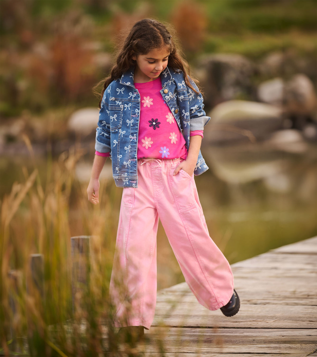 Girl modeling a blue bow-print slouchy denim jacket with rolled cuffs and brass-tone buttons