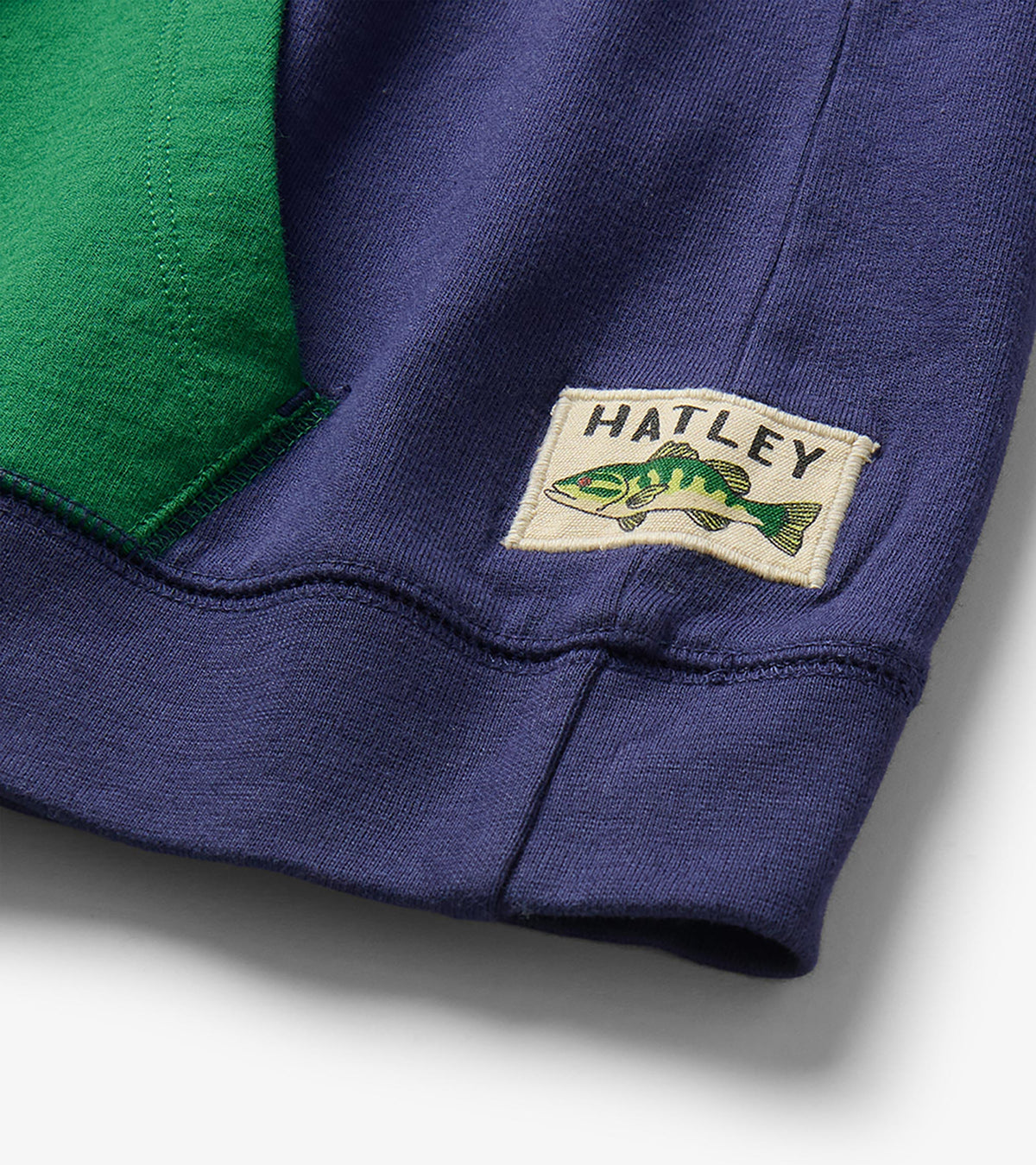 Close-up of hem on blue hoodie with green pocket and visible Hatley fish patch