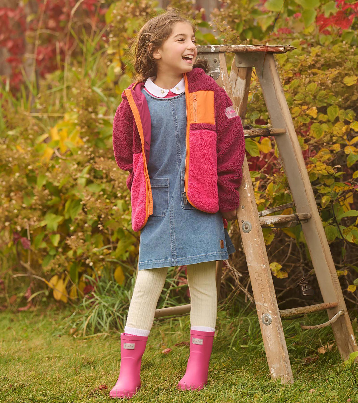 Girl outdoors wearing bright pink rain boots with a denim dress and colorblock fleece jacket