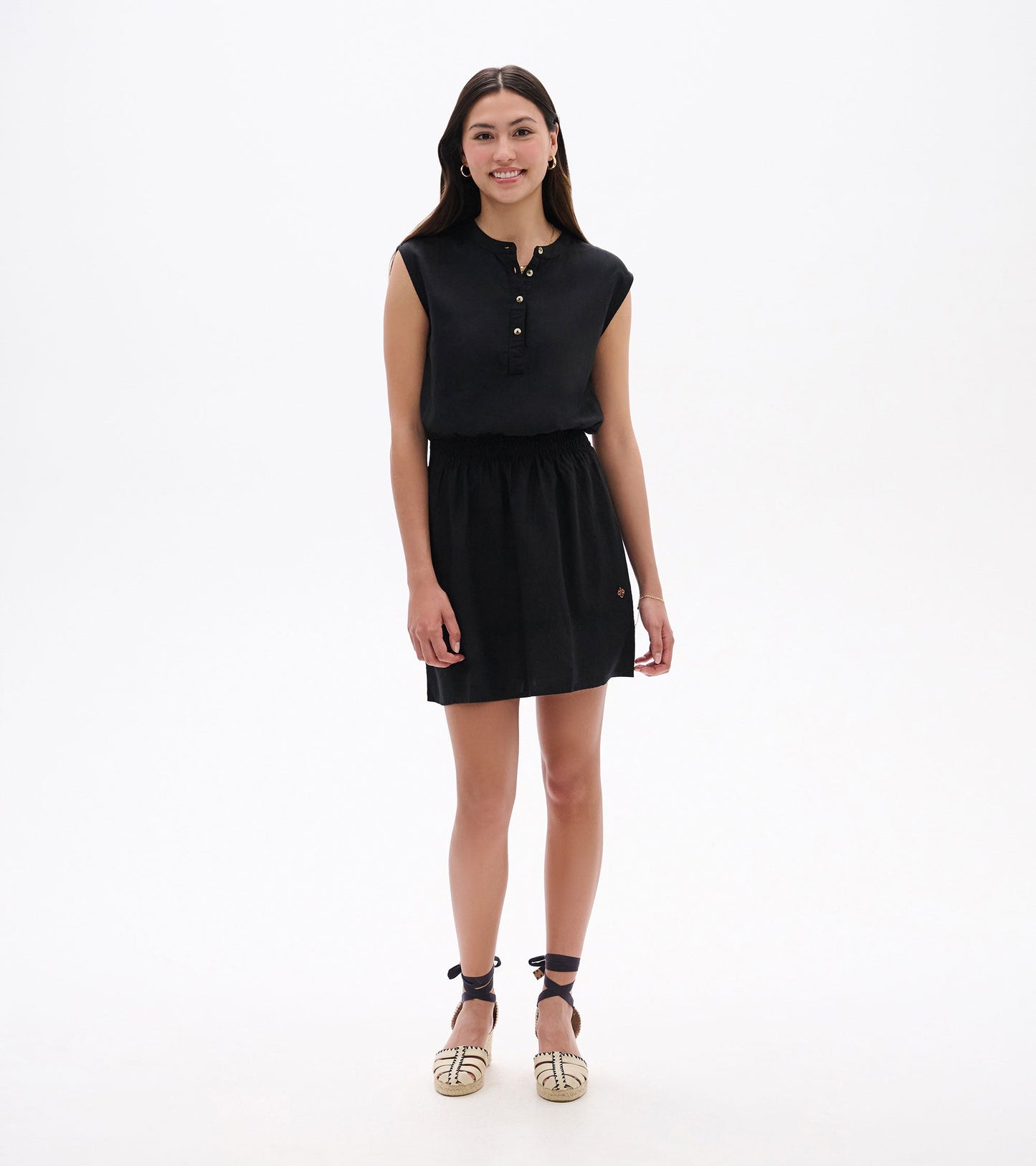 Black sleeveless dress with a buttoned neckline and elastic waist, styled with espadrille sandals.