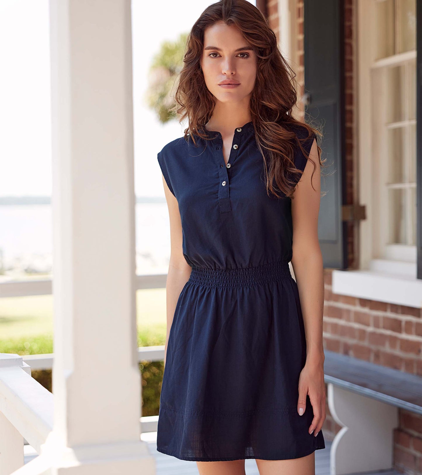 Black sleeveless dress with a buttoned collar and smocked waist, styled for a casual look.
