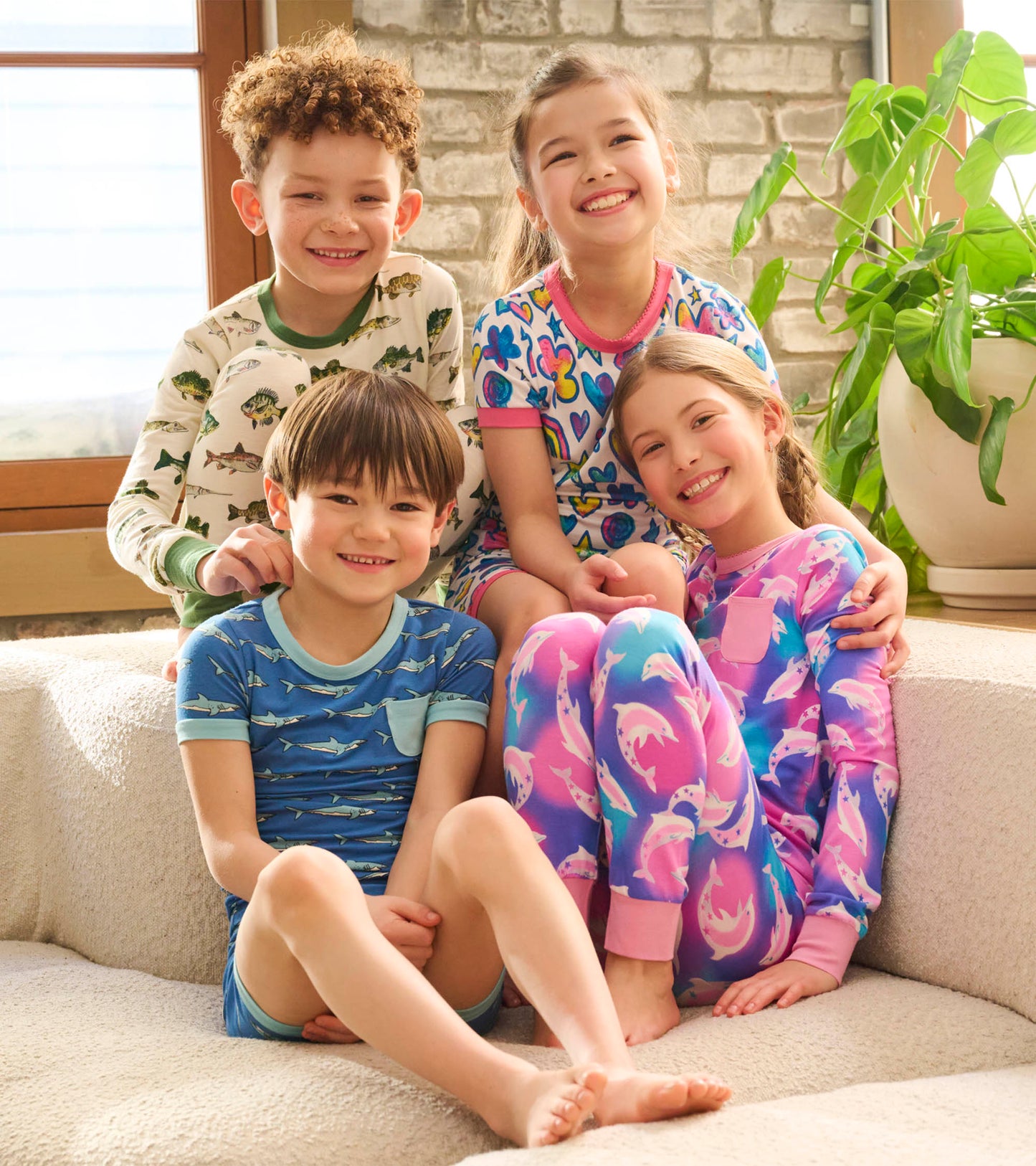 Colorful bamboo pyjama set featuring dolphin patterns, worn by four children sitting together on a cozy couch.
