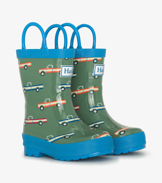 Green wellies featuring colorful truck patterns and blue handles, designed for toddlers and kids.