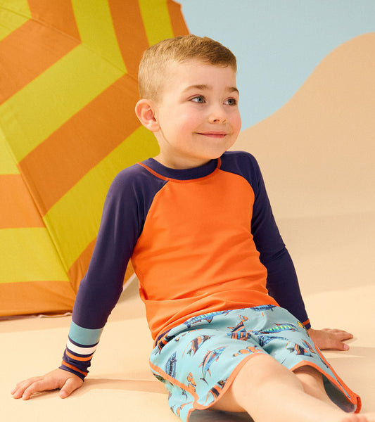 Bright orange long sleeve rashguard with navy sleeves, perfect for beach activities, worn by a smiling boy.