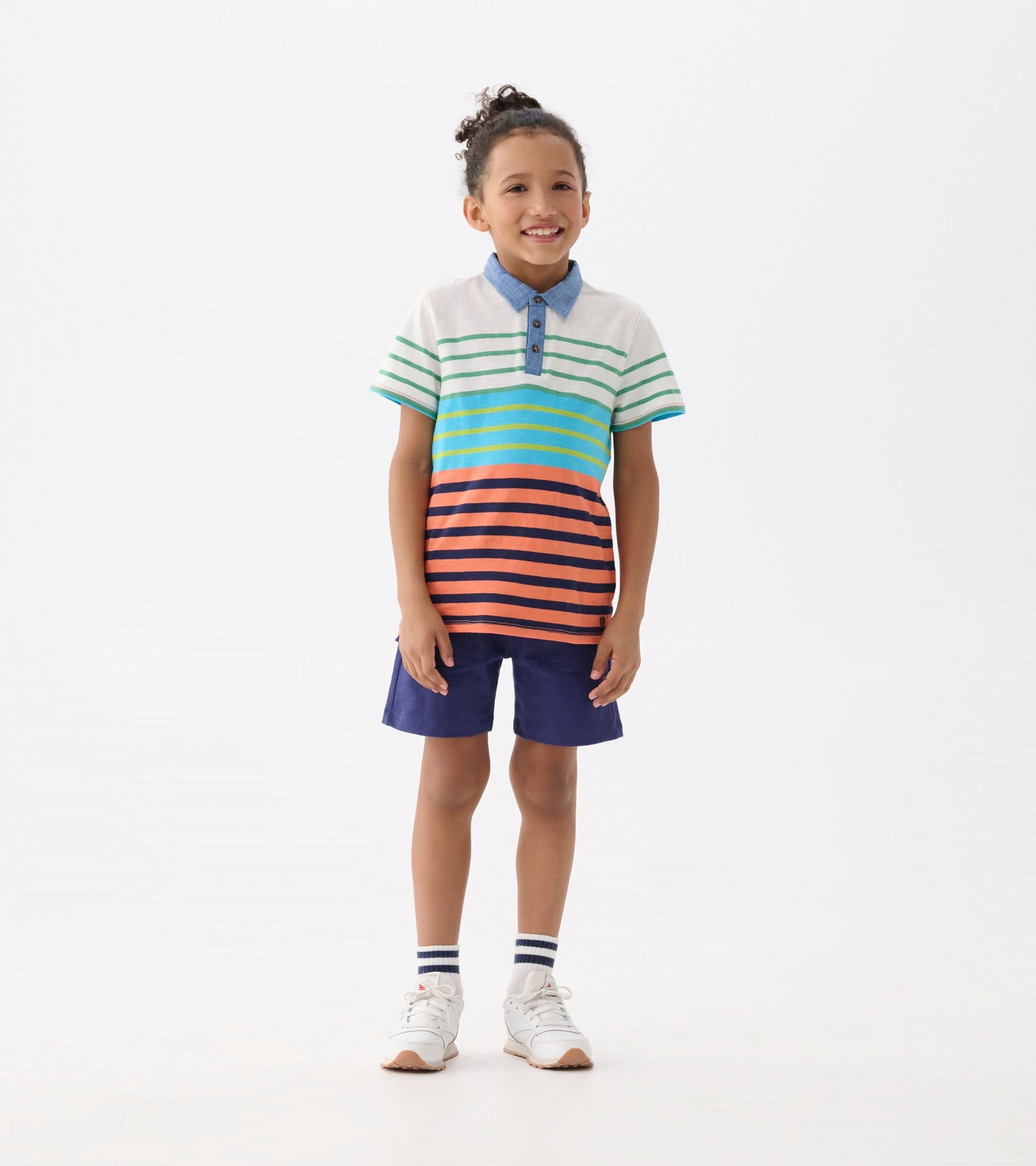 Multicolored striped polo tee with a denim collar, paired with navy shorts, worn by a smiling boy.