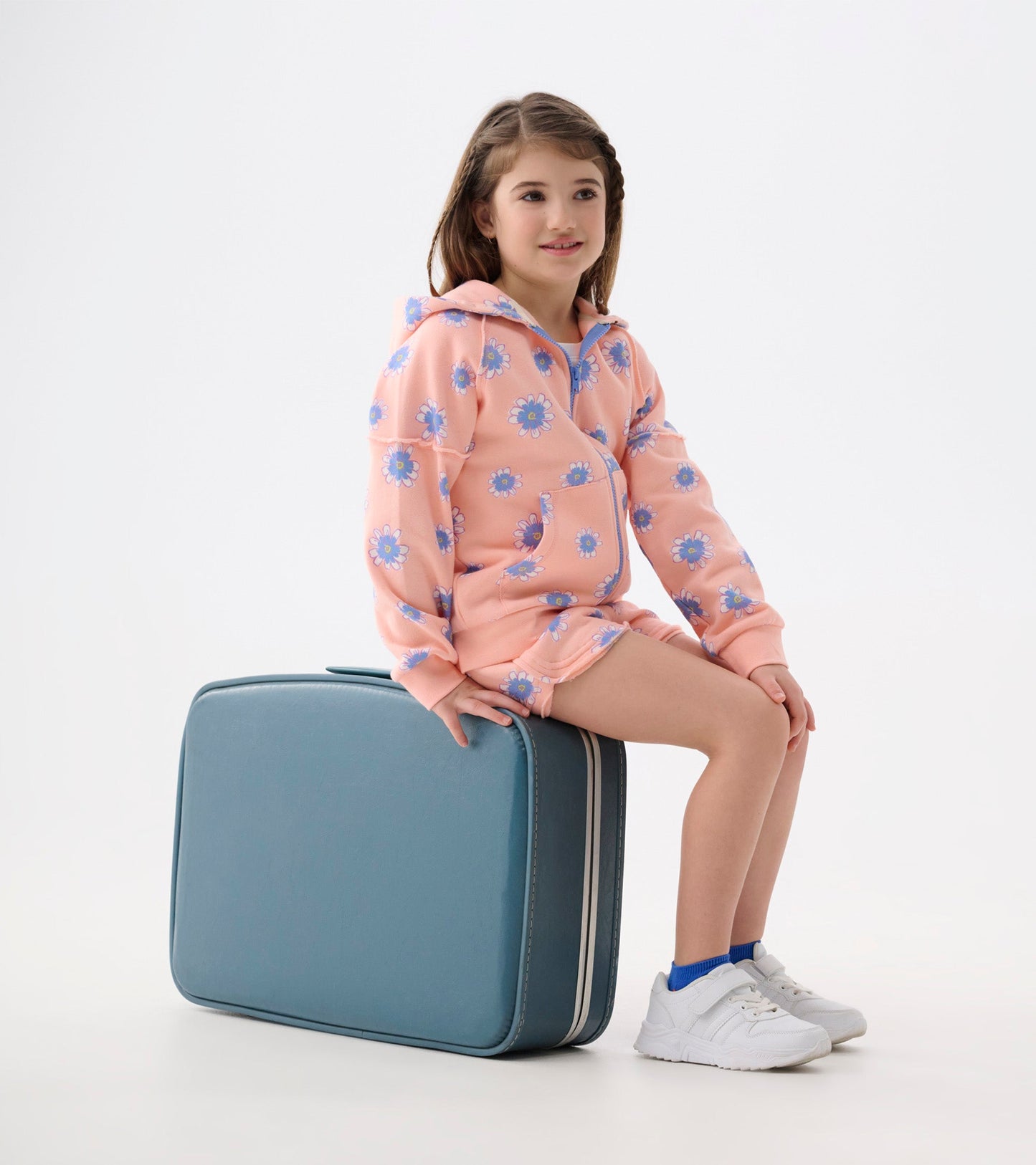 Pink hoodie with blue daisy pattern, front pocket, and hood, worn by a girl sitting on a teal suitcase.