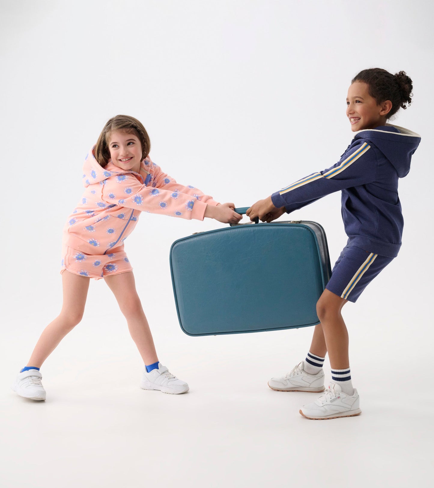 Pink hoodie with blue daisy pattern, worn by a girl, as she plays with a boy holding a teal suitcase.