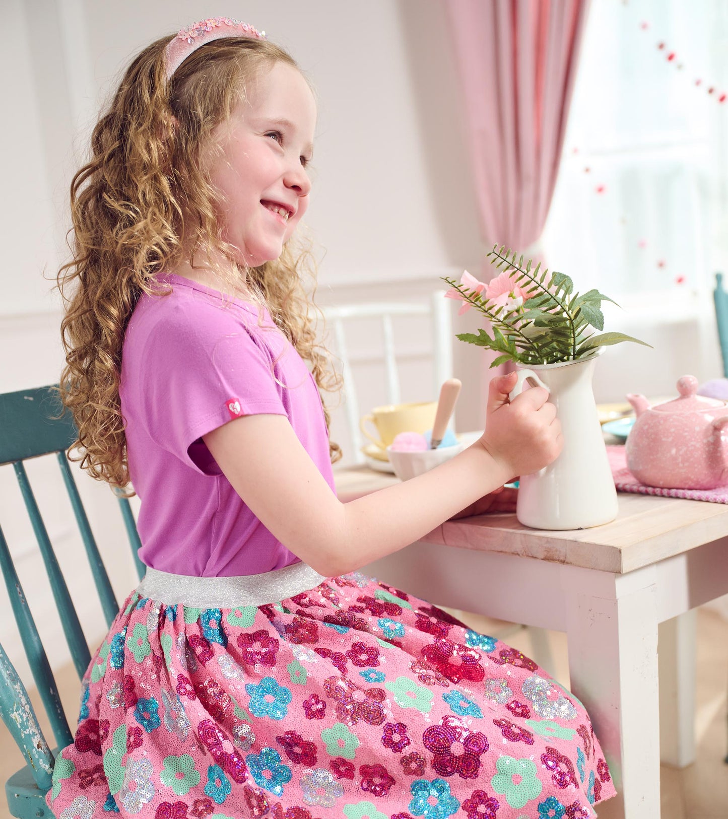 Pink tulle skirt with colorful daisy sequins, paired with a purple top, worn by a girl at a table.