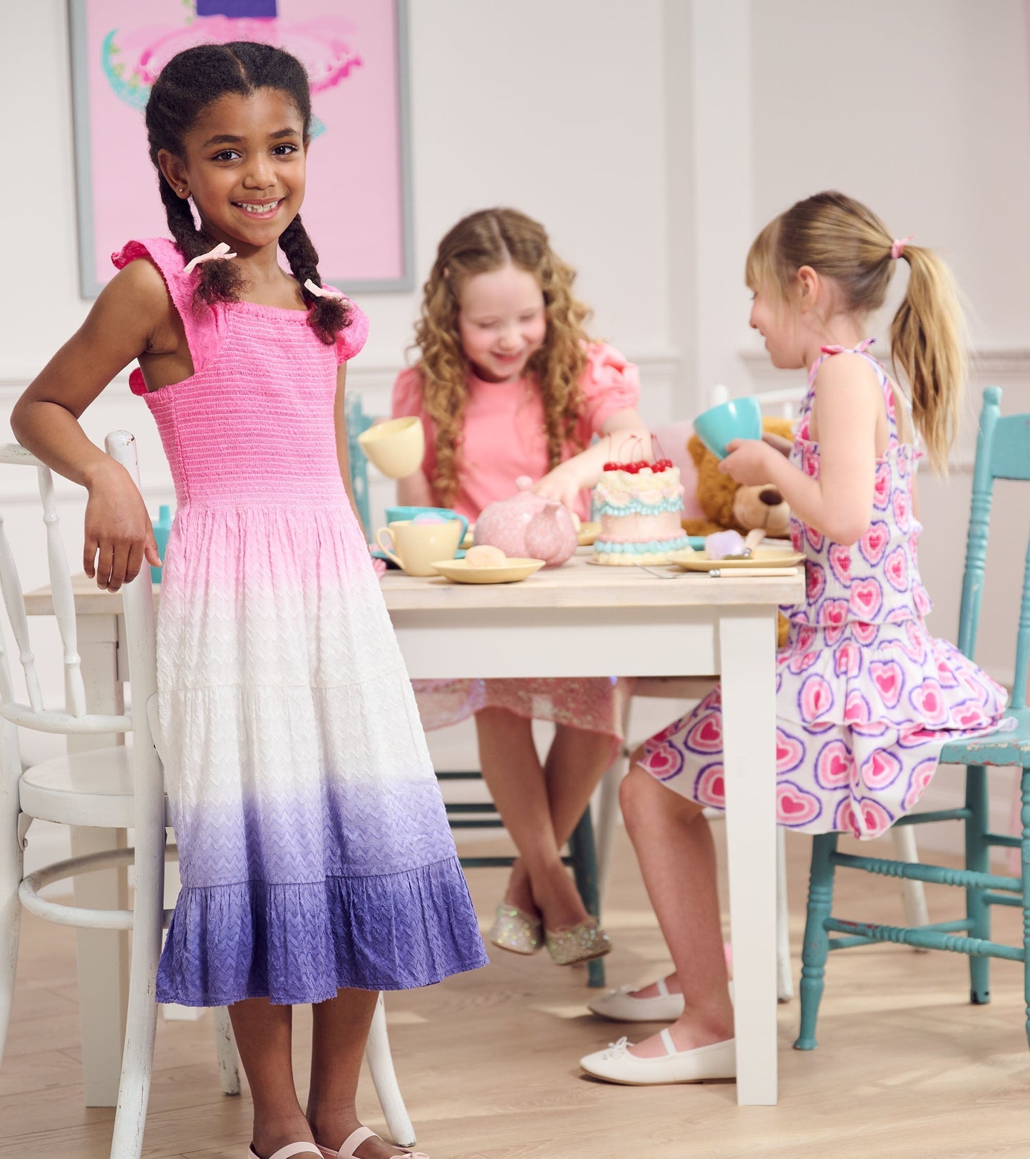 Smocked angel dress featuring a gradient of pink to white to purple, with ruffled straps, worn by a girl at a tea party.