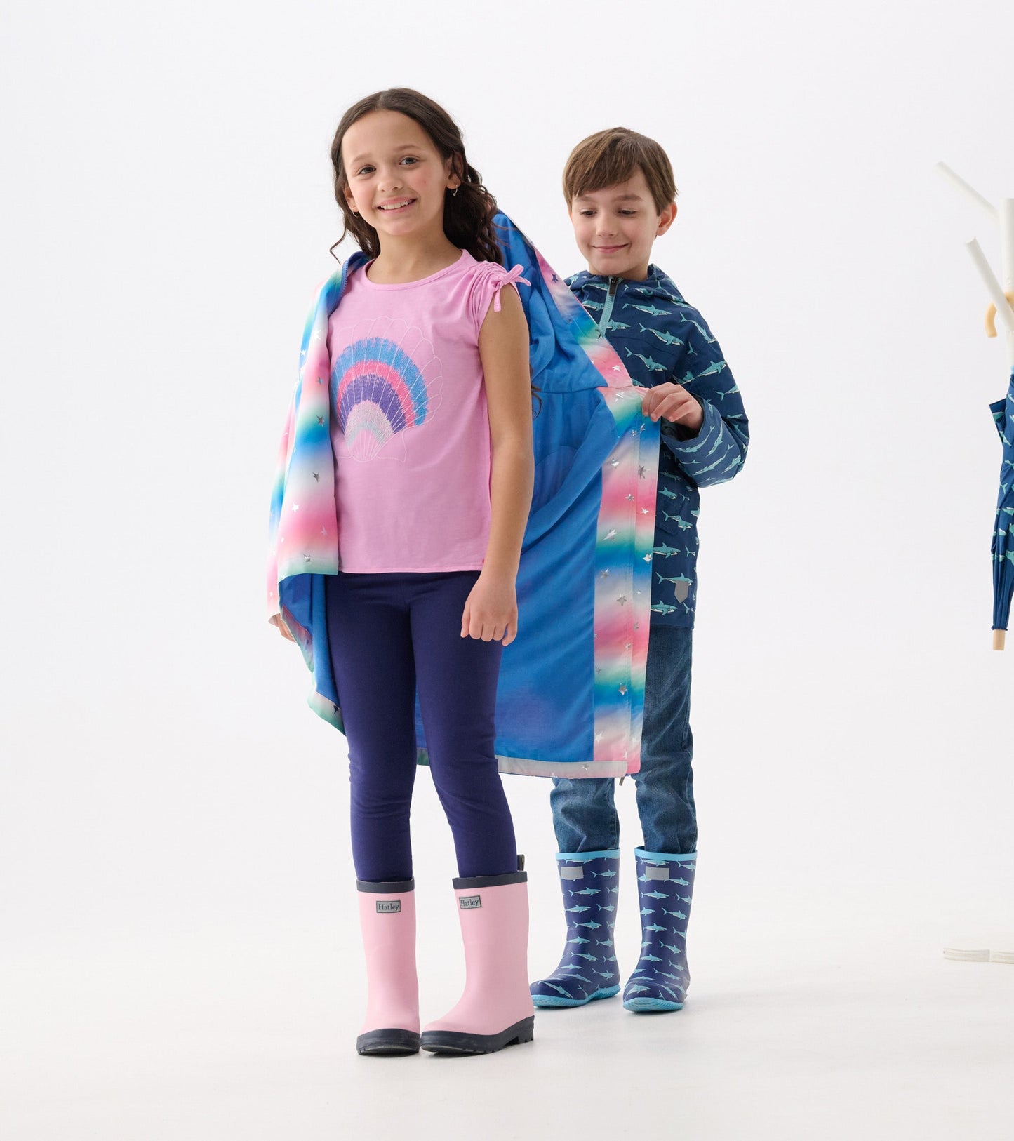 A girl in a pink top and leggings wears a colorful glitter star A-line swing jacket, while a boy assists her.